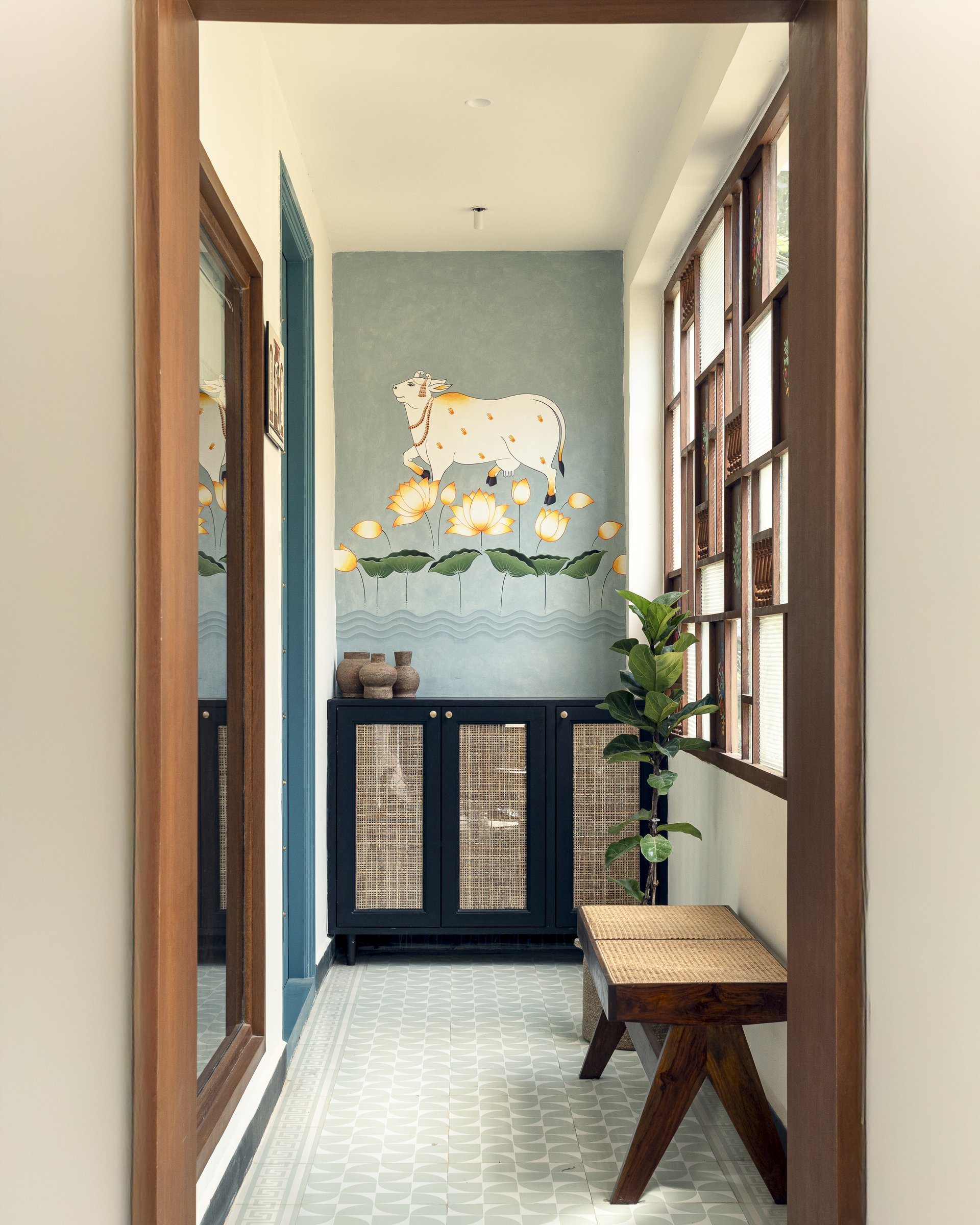 The foyer, where a hand-painted Pichwai mural and geometric cement tiles set the home's South Indian register before a single room reveals itself
