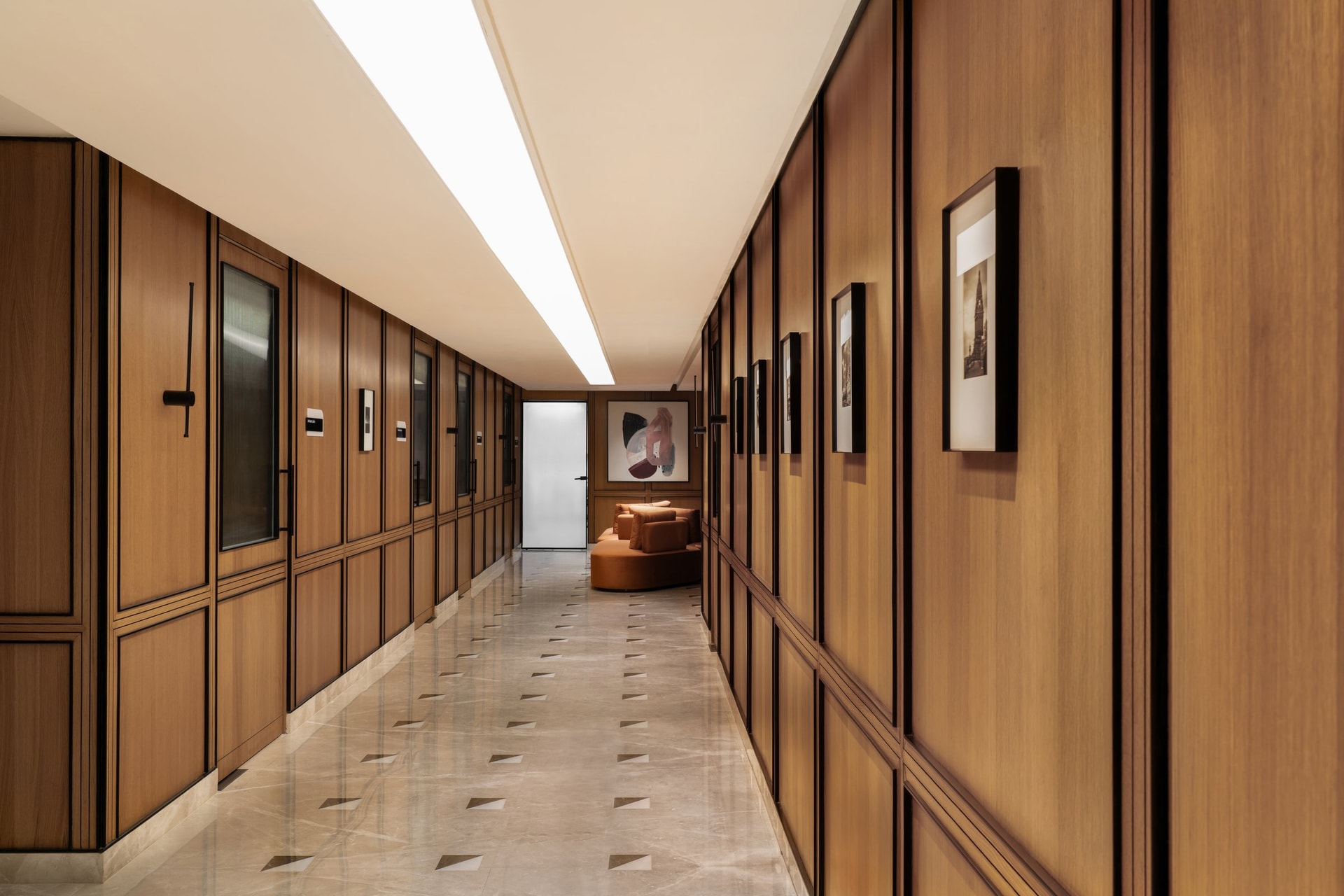 Further along the corridor, framed works and a rust-orange sofa anchor the passage