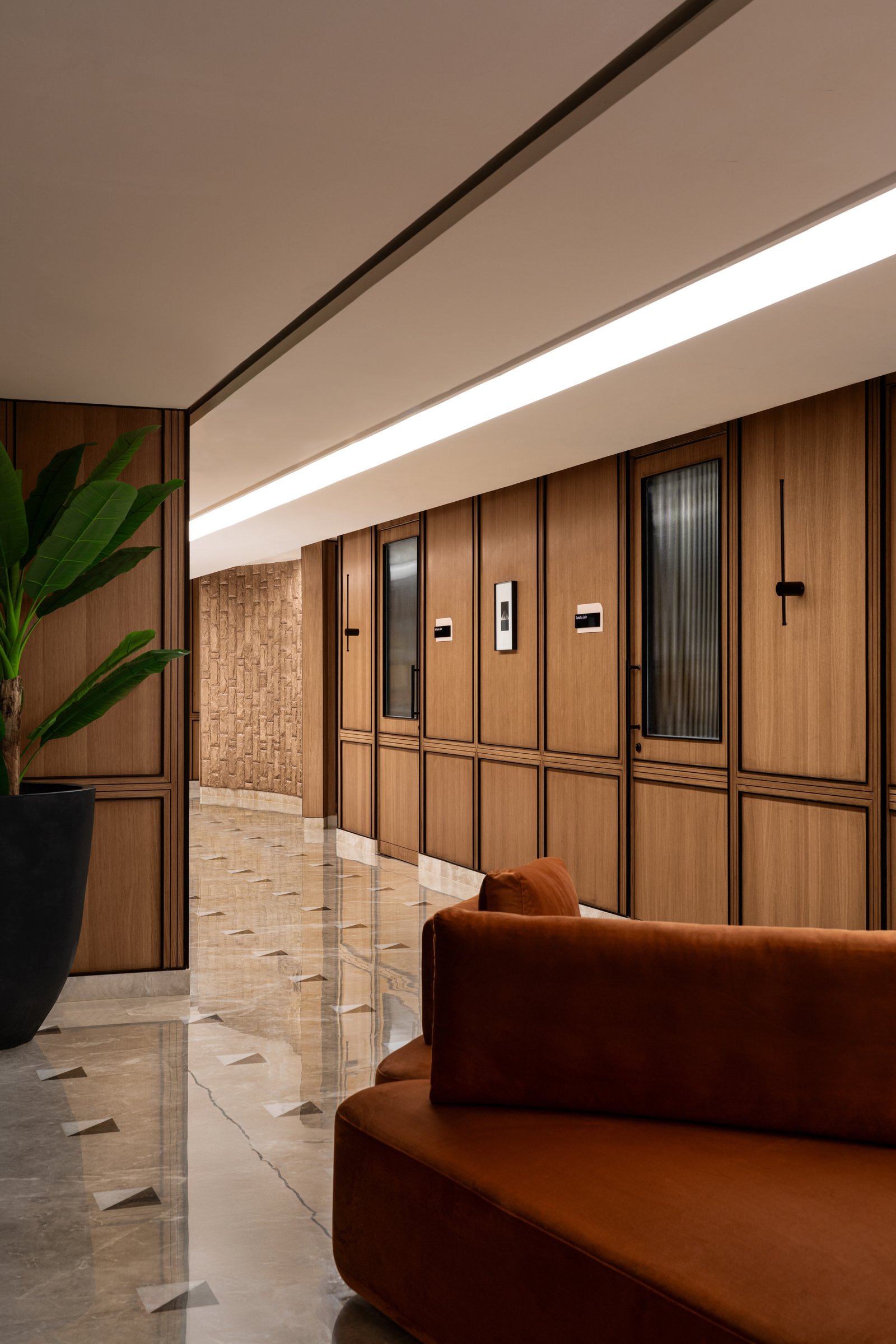 The same corridor in reverse, a continuous linear ceiling fixture holding the long axis together