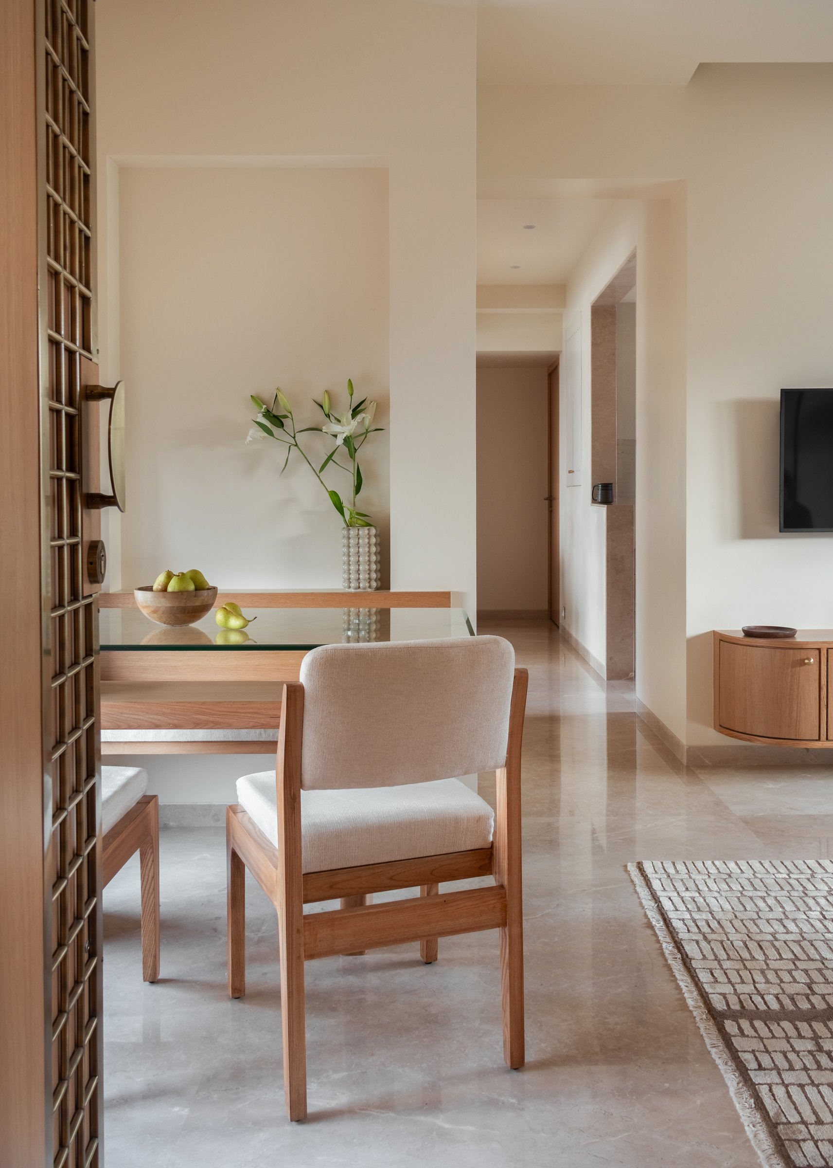 The dining niche just inside the front door, where a glass-topped wooden table and upholstered chairs occupy a recess that reads as a room