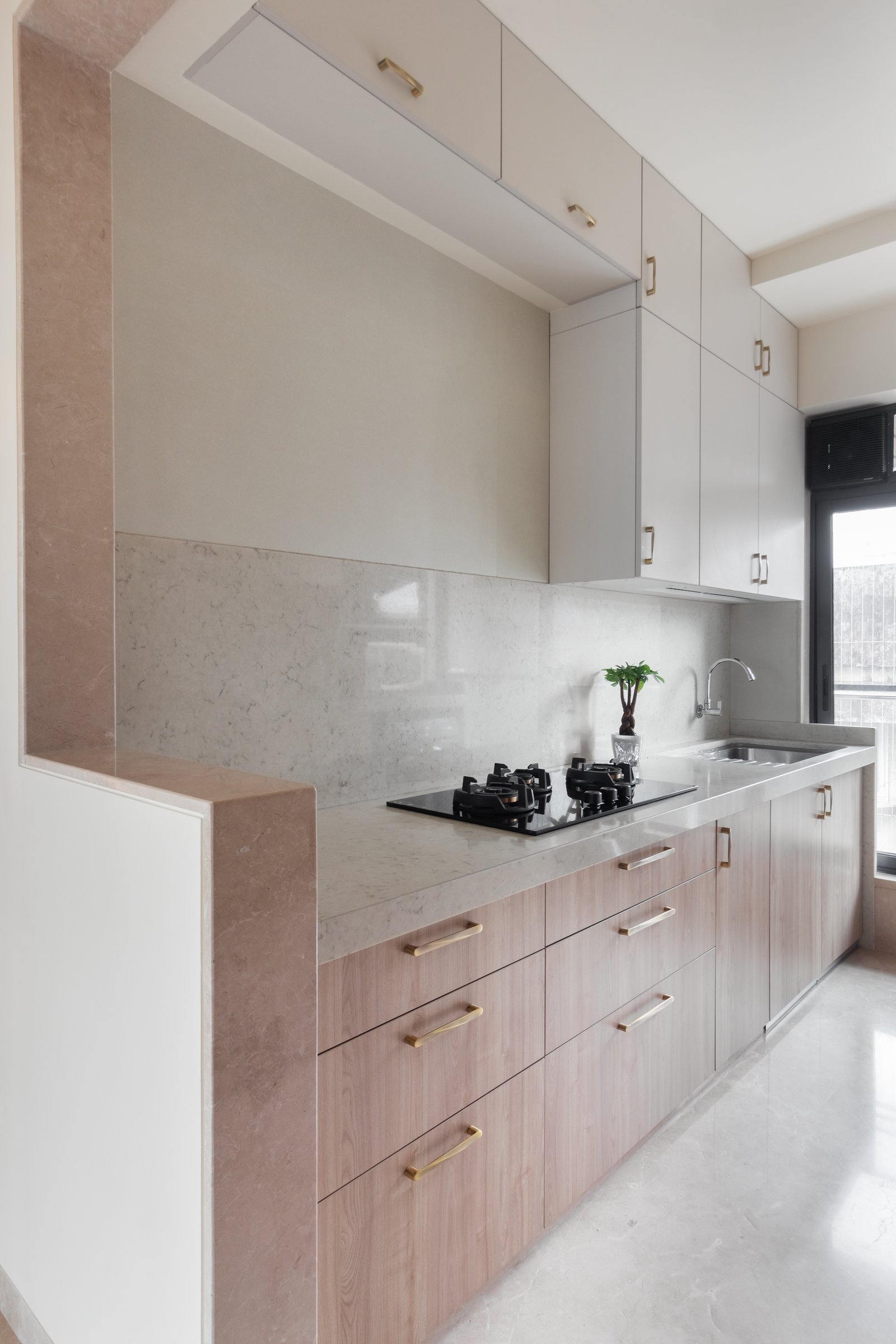 The galley kitchen, where pale oak lowers, soft off-white uppers, and a vertical band of warmer stone define the threshold to the living area