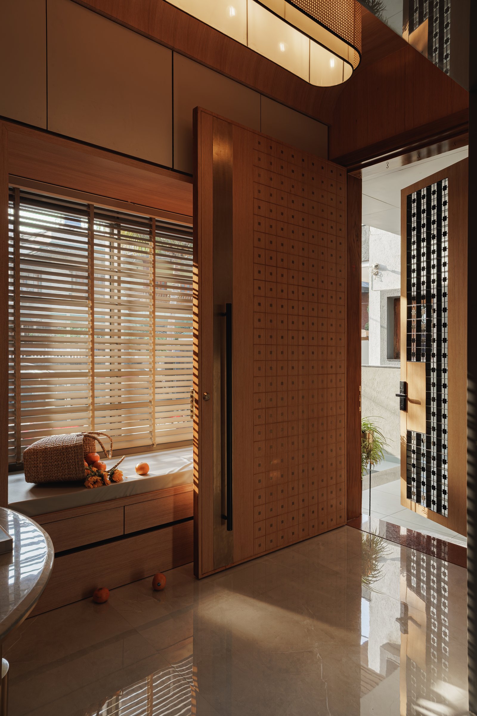 The foyer, where a perforated wood pivot door and a built-in window seat give arrival its own small room