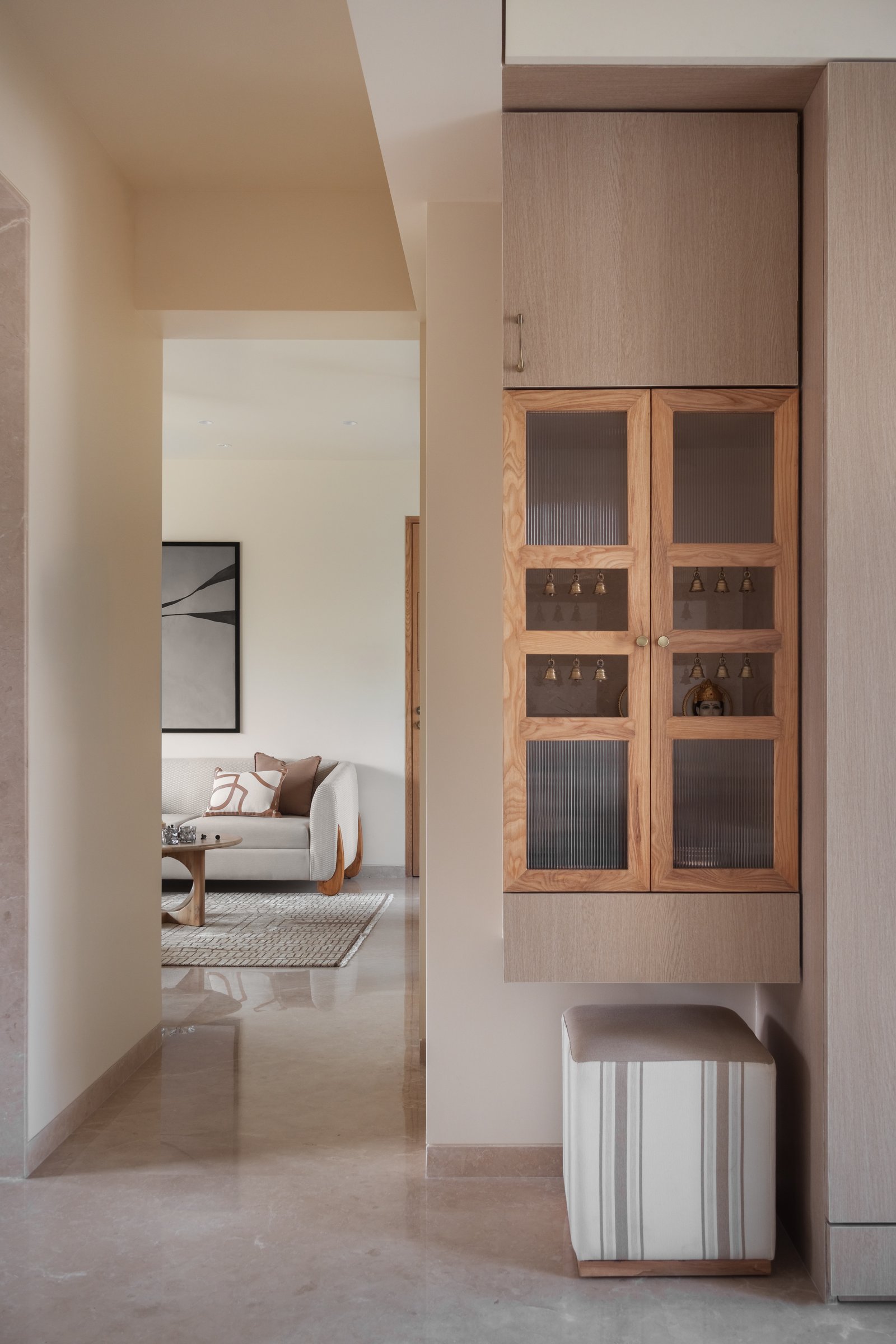 The pooja niche just inside the entry, where reeded glass and small brass bells fold ritual into the home's everyday circulation