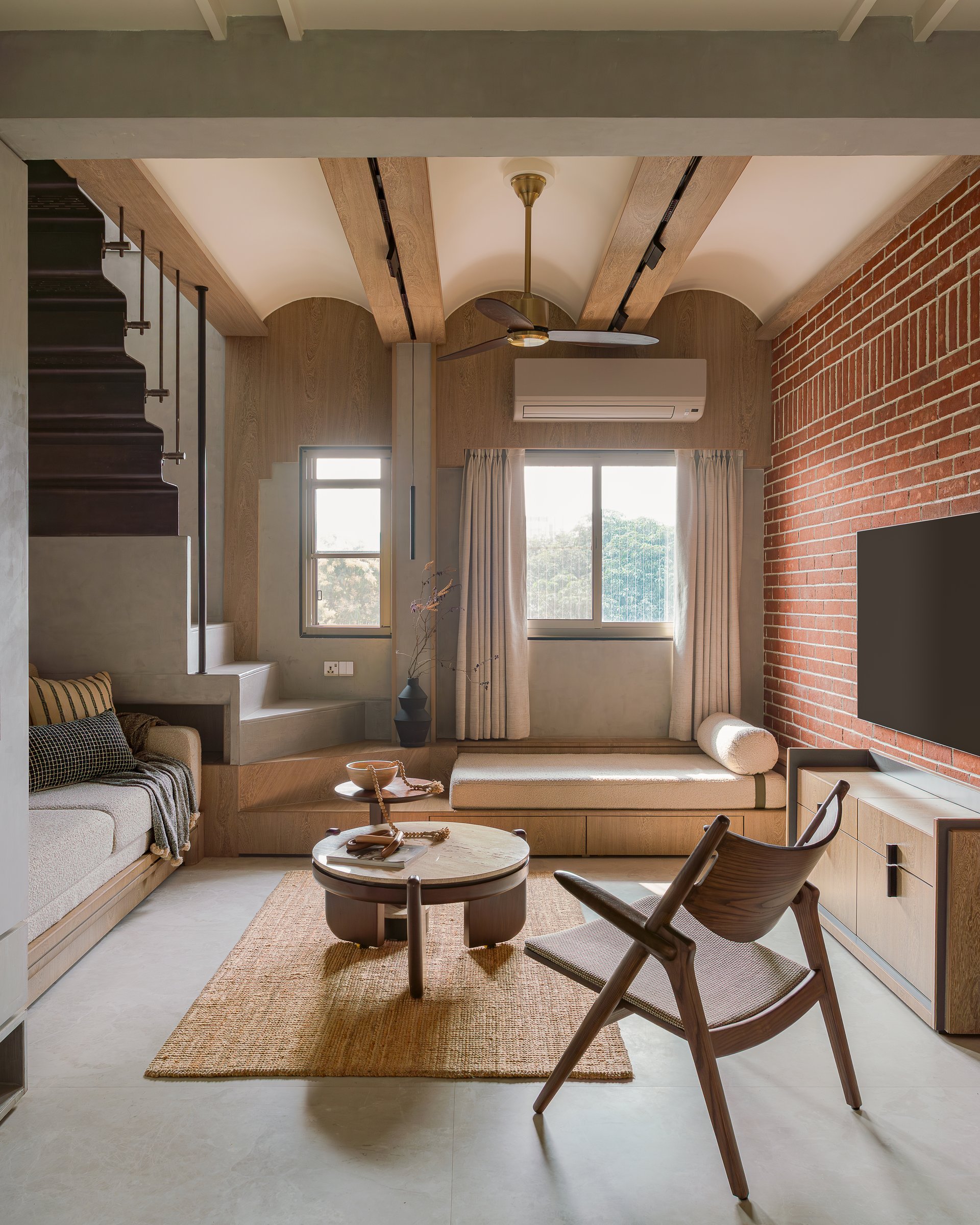 The living room, where red brick and pale wood hold a deliberate argument across a single, generous frame