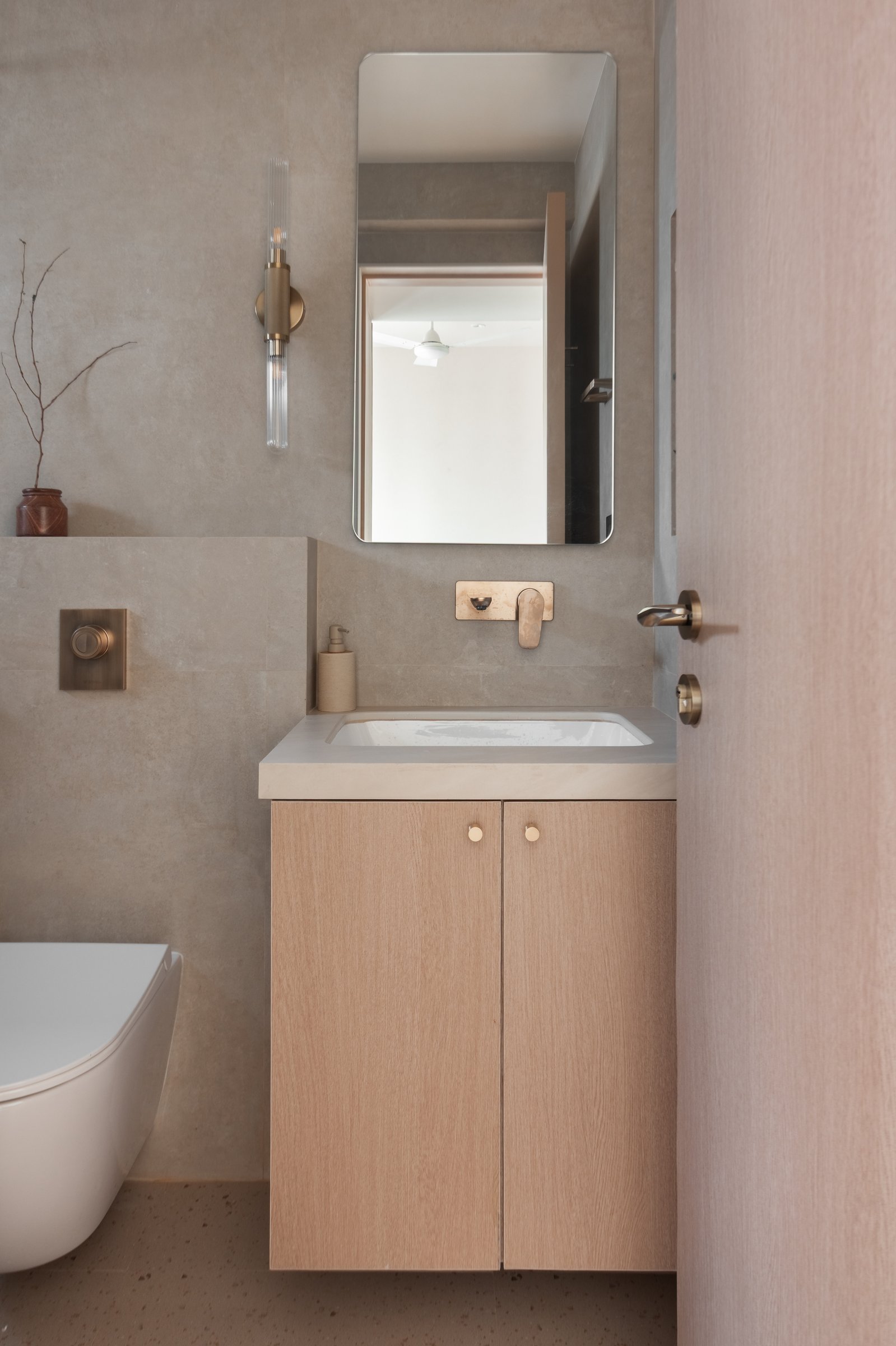 The guest bathroom, where a floating oak vanity and brass-and-glass sconce carry the apartment's restraint into its smallest room