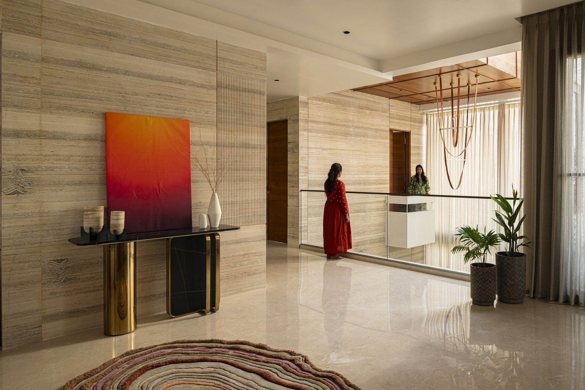 The upper lobby, where a travertine wall and a brass-and-stone console establish the home's material grammar before any room is entered