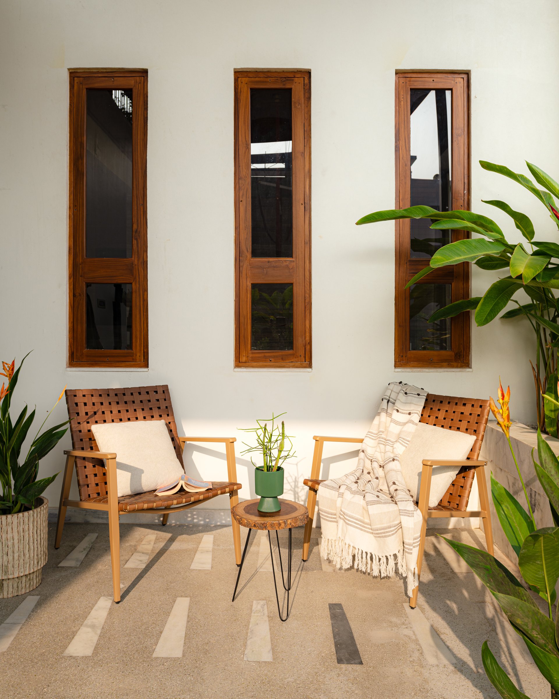 A ground-level courtyard, with woven-leather lounge chairs and a live-edge side table beneath three teak-framed windows