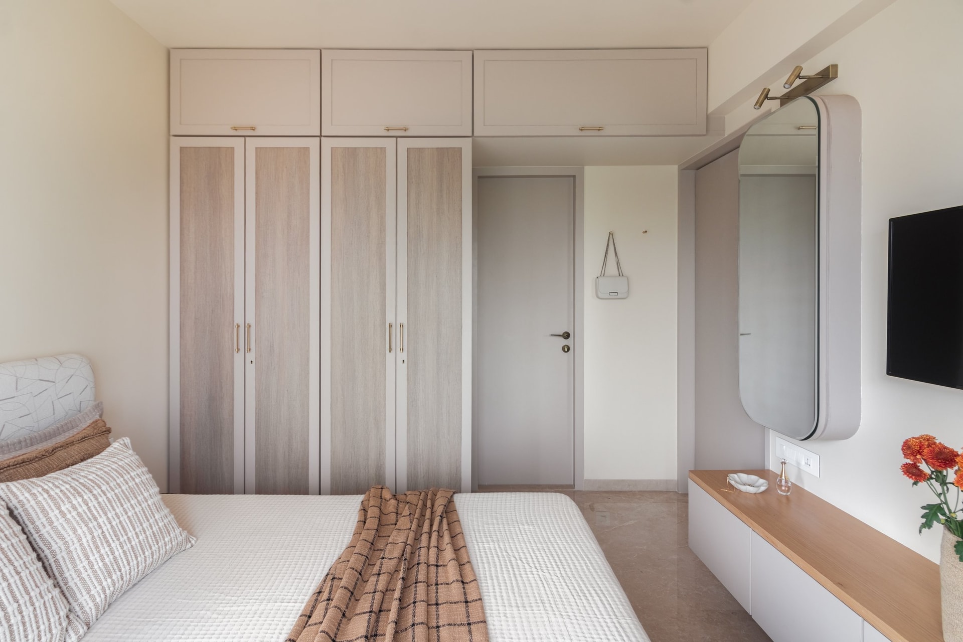 Opposite the master bed, a wall of pale oak and soft off-white joinery absorbs the room's storage entirely into the architectural shell