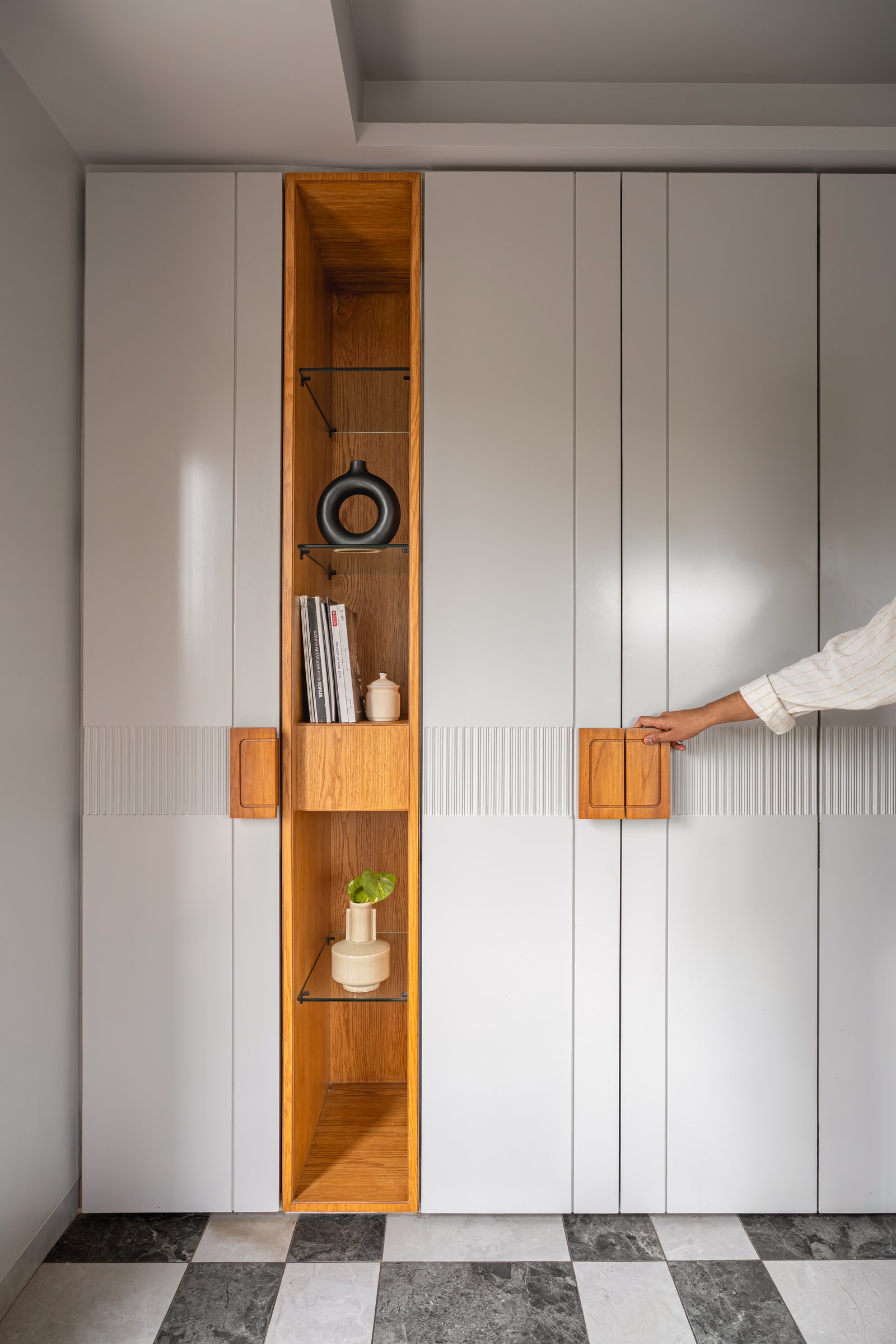The storage wall: full-height pale wardrobes broken by a single vertical niche of warm wood