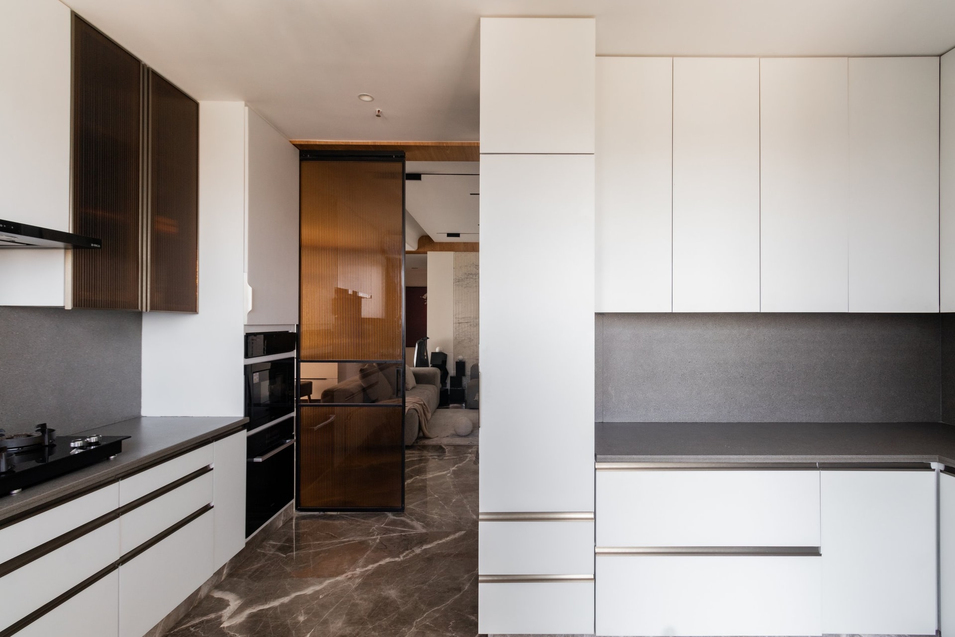 The kitchen threshold, where a sliding amber reeded-glass door preserves continuity with the social zones
