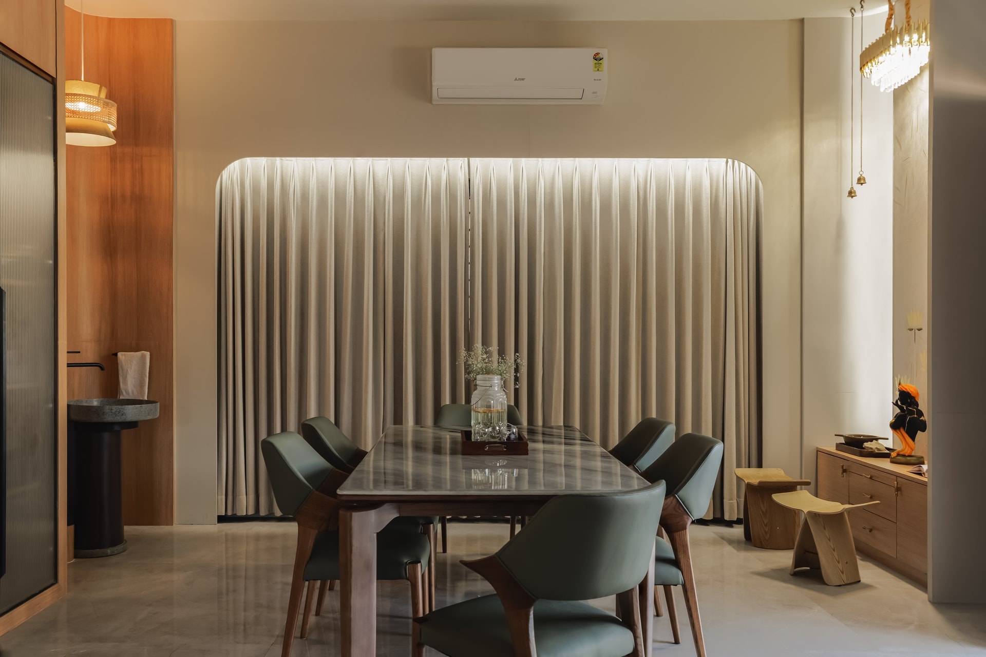 The dining room, where backlit pleated drapery glows behind a slim marble table and sage-leather chairs
