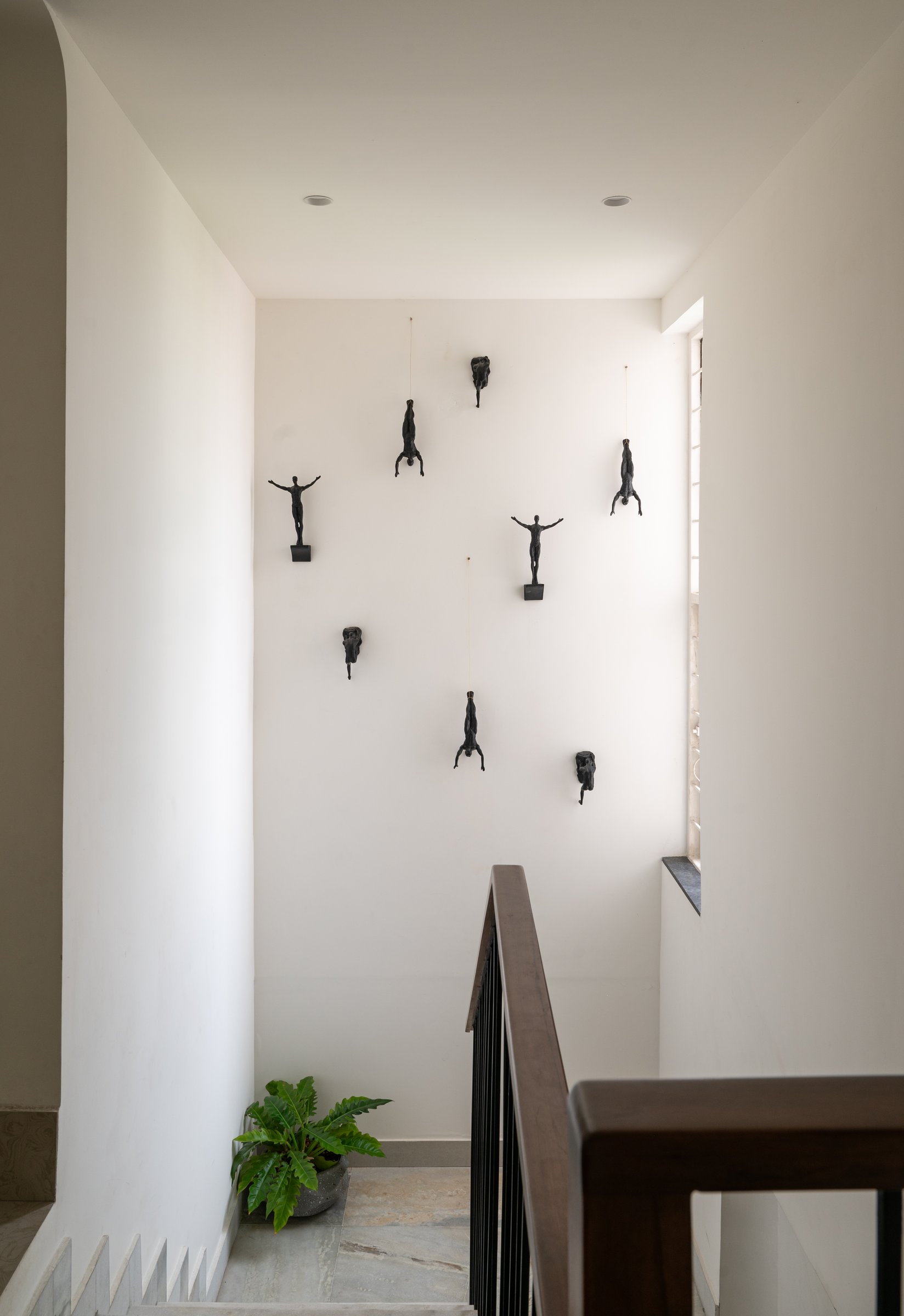 The stairwell, where small bronze figures scale the white wall in a loose, choreographed climb