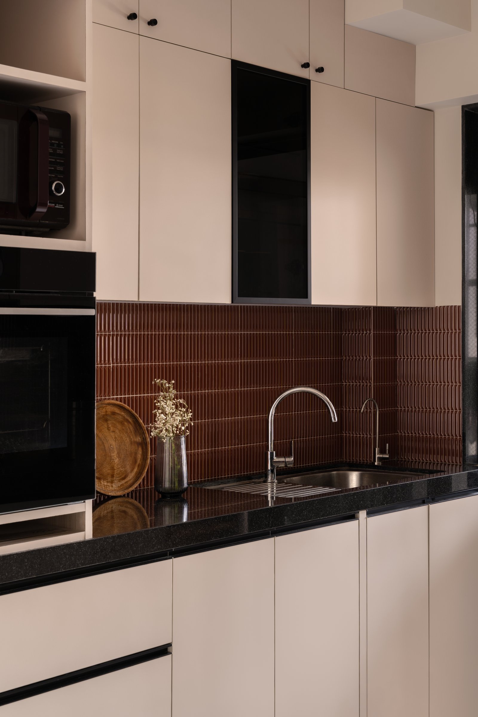 The kitchen, where cream cabinetry meets an oxblood ribbed backsplash and a black stone counter in a compressed version of the home's palette