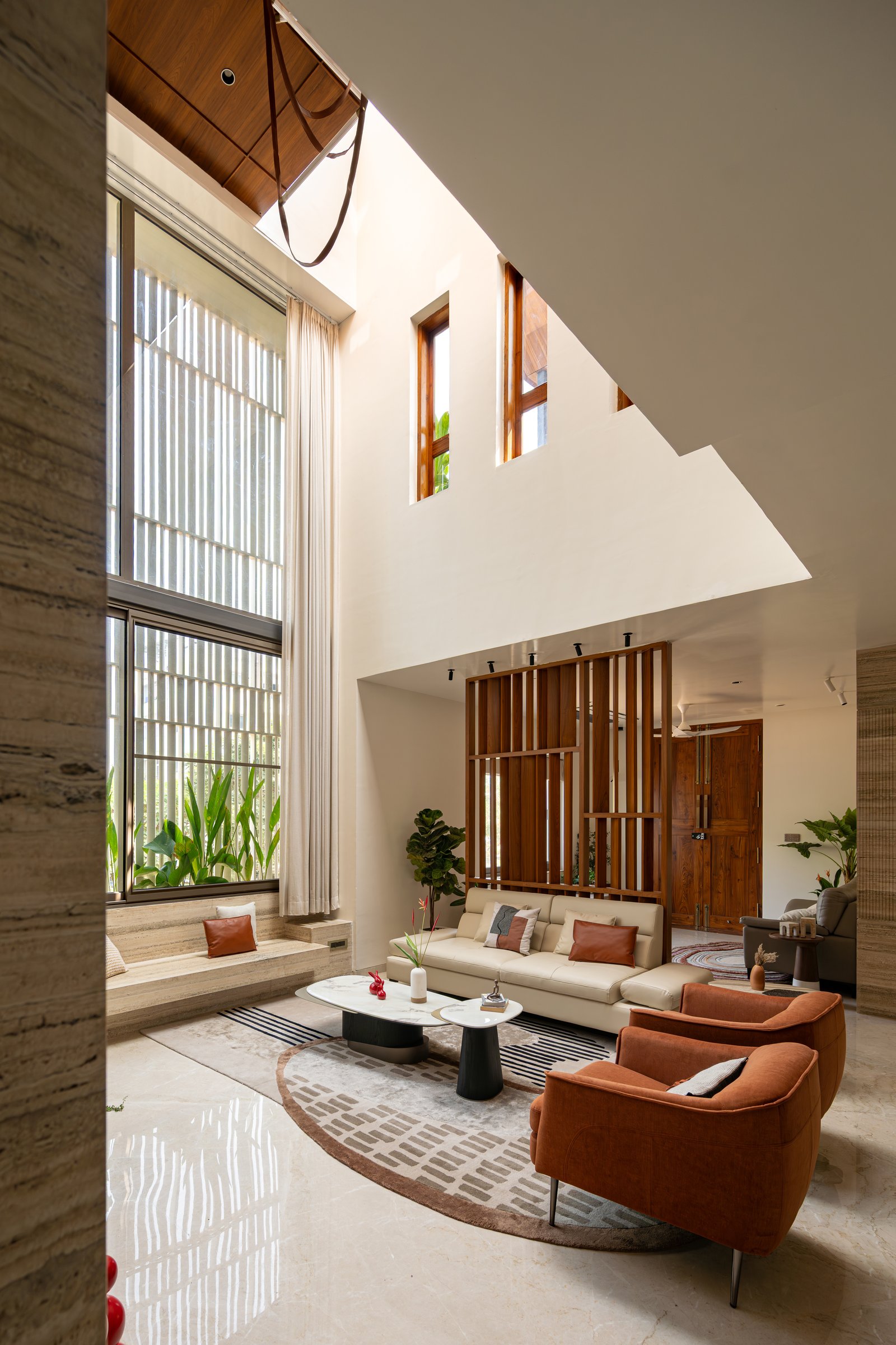 Seen from the entry, the living room reveals a slatted teak screen and a stepped stone bench beneath full-height glazing