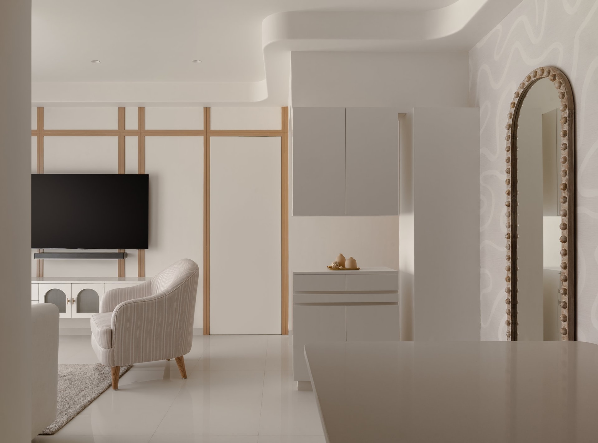The open plan, where a striped armchair and a battened media wall hold the apartment's neutral key