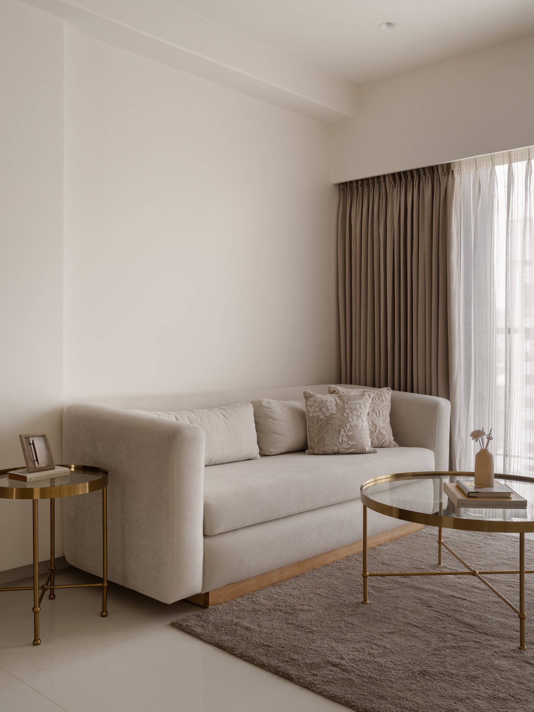 The living room, where a pale three-seater and brass side tables compose the apartment's quietest moment