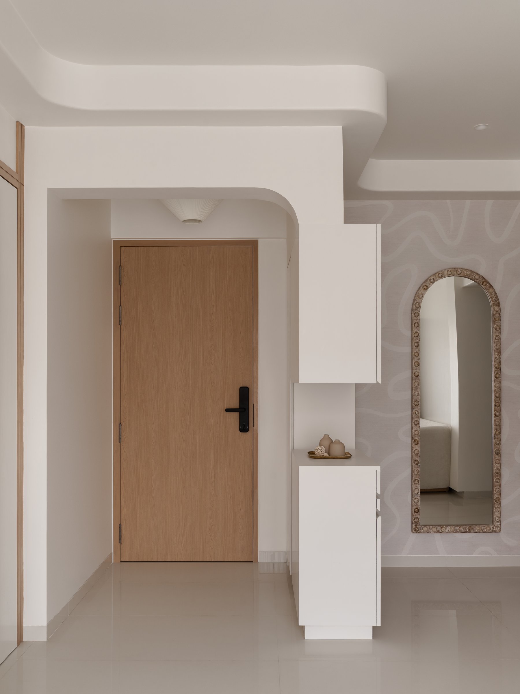 The entry, where a wood-grain door, a slim white console, and an arched mirror set the home's measured opening gesture