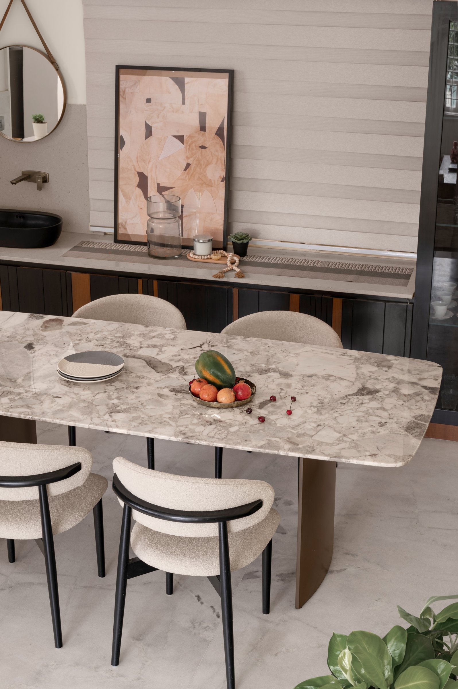 The dining table in veined stone, seen from the side that faces the cabinetry and a framed collage in soft terracotta tones