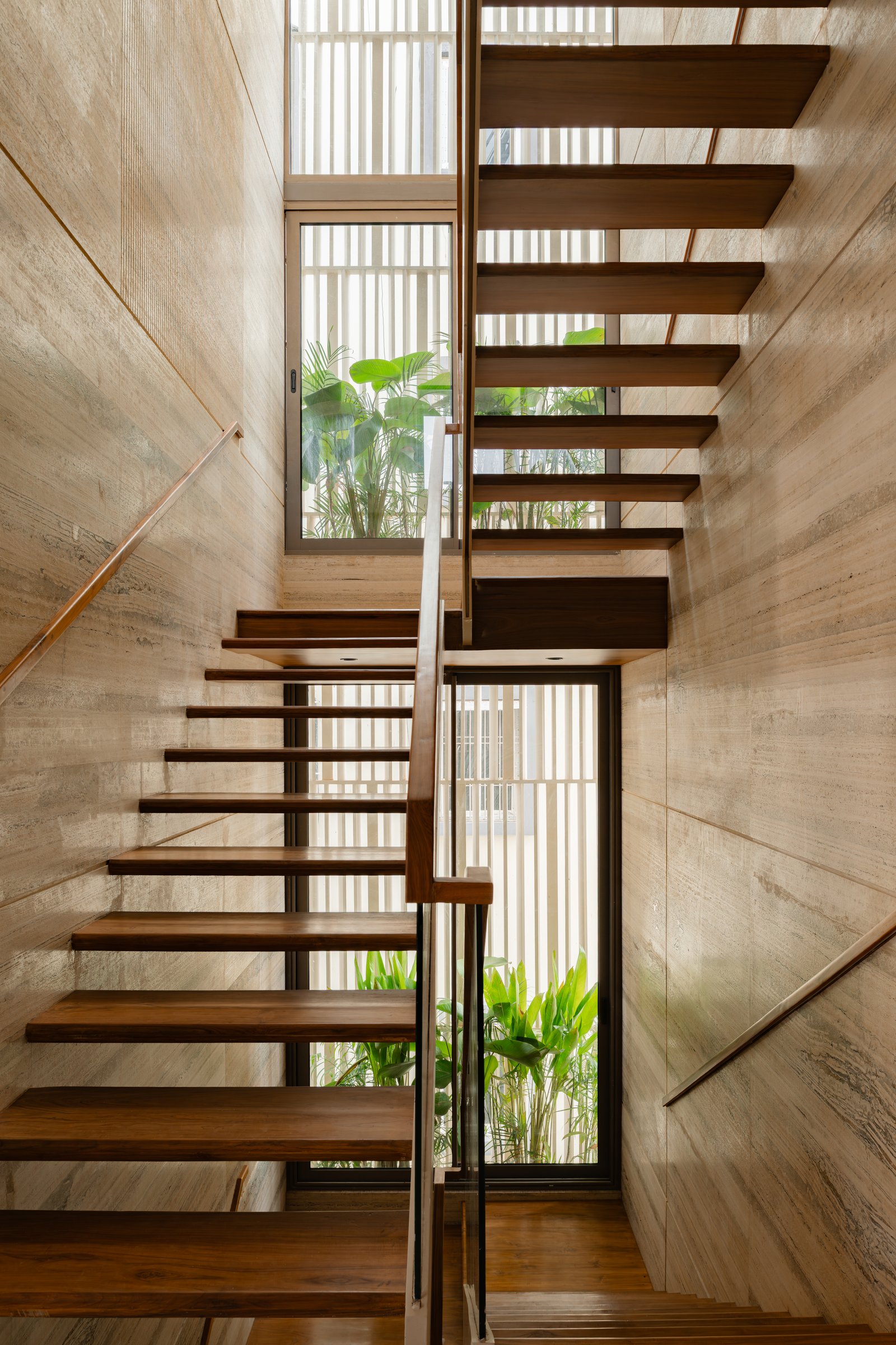 The staircase: cantilevered teak treads floating against full-height travertine walls