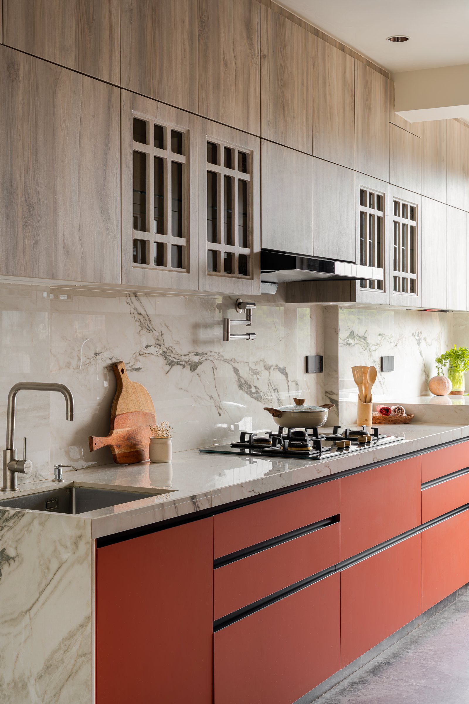 The kitchen's one registered note of colour: terracotta-red lowers against veined stone and mullioned upper cabinetry