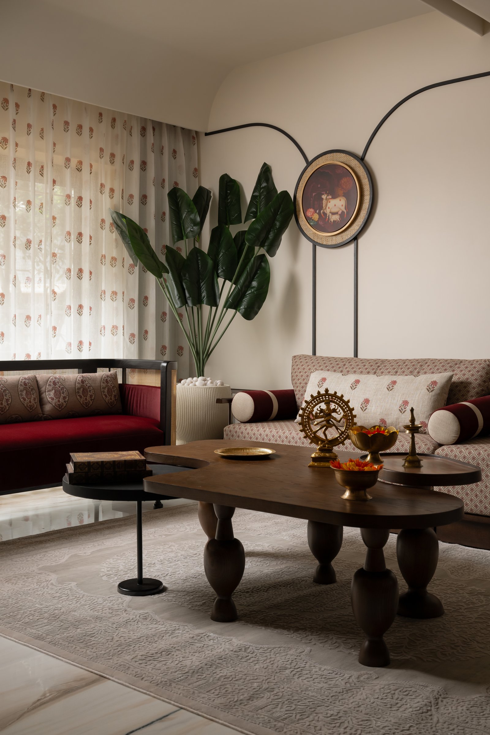 The living room from a second vantage, with a deep red settee beneath a slim black linework loop framing a pichwai-style artwork