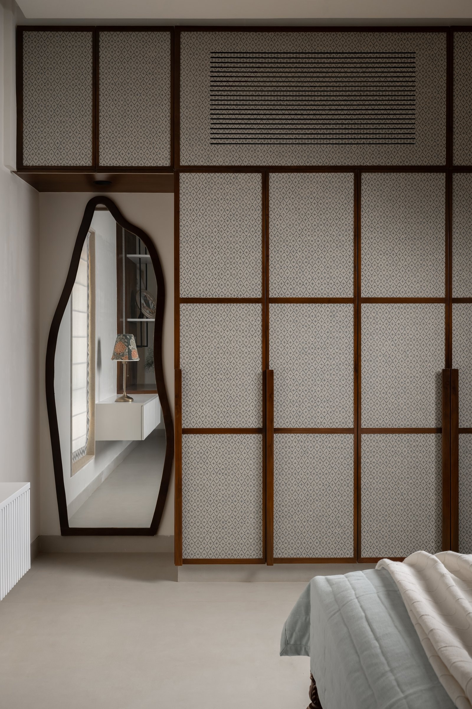 A wall of wardrobes faced in diamond-patterned upholstery, with a wave-edged mirror against the adjacent wall