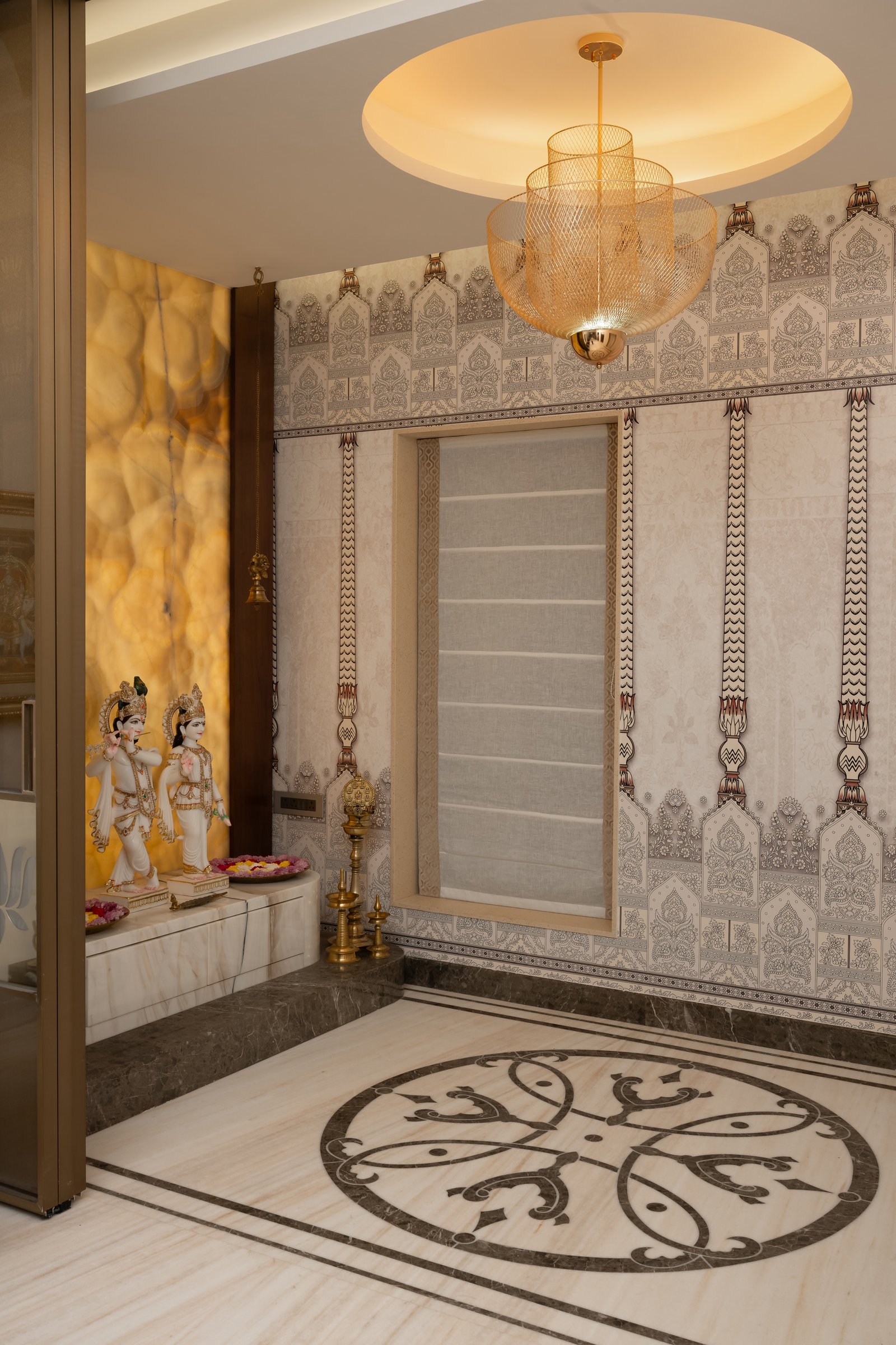 The temple room, with backlit amber onyx behind the marble murtis and a woven gold pendant overhead