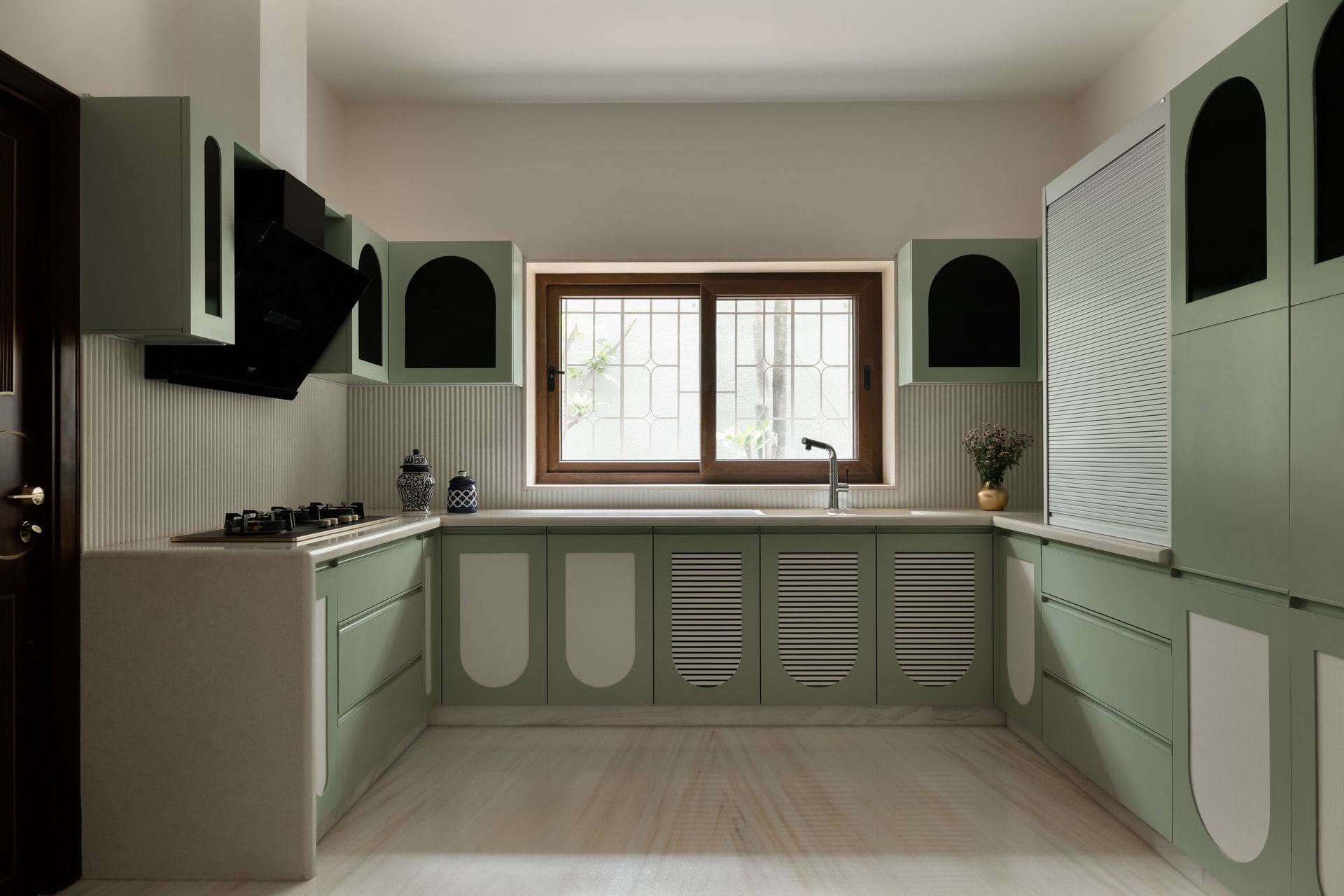 The kitchen, where sage green cabinetry with arched insets carries the home's arch motif into a more graphic key