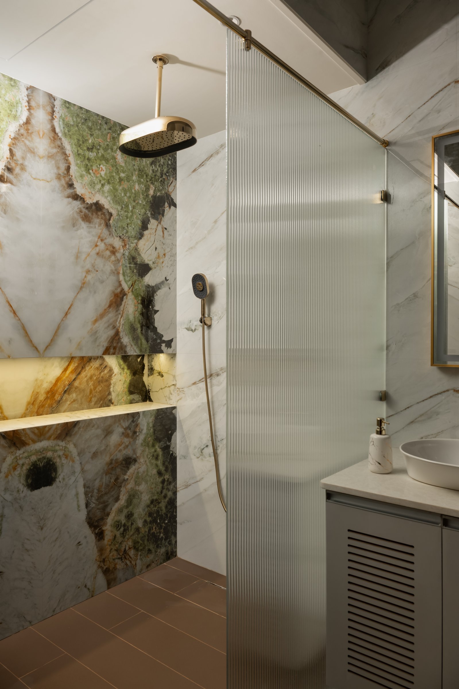 The primary bathroom, where a slab of patterned quartzite reads as landscape behind a reeded glass shower screen