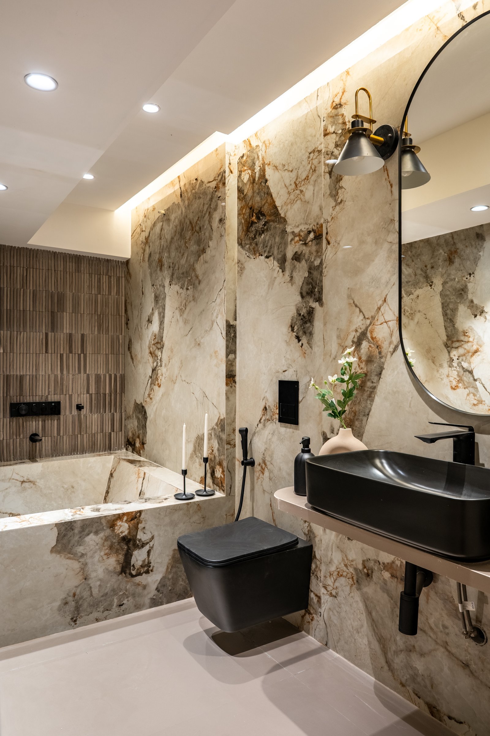 The principal bathroom, where dramatic veined stone wraps the walls and tub against matte black fixtures