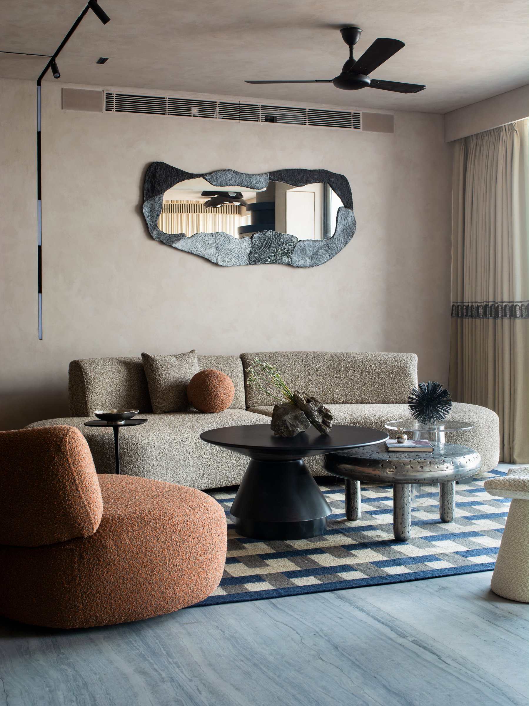 Boucle seating in oatmeal and burnt orange anchored by a geometric blue-and-cream rug, with an irregularly framed sculptural mirror above