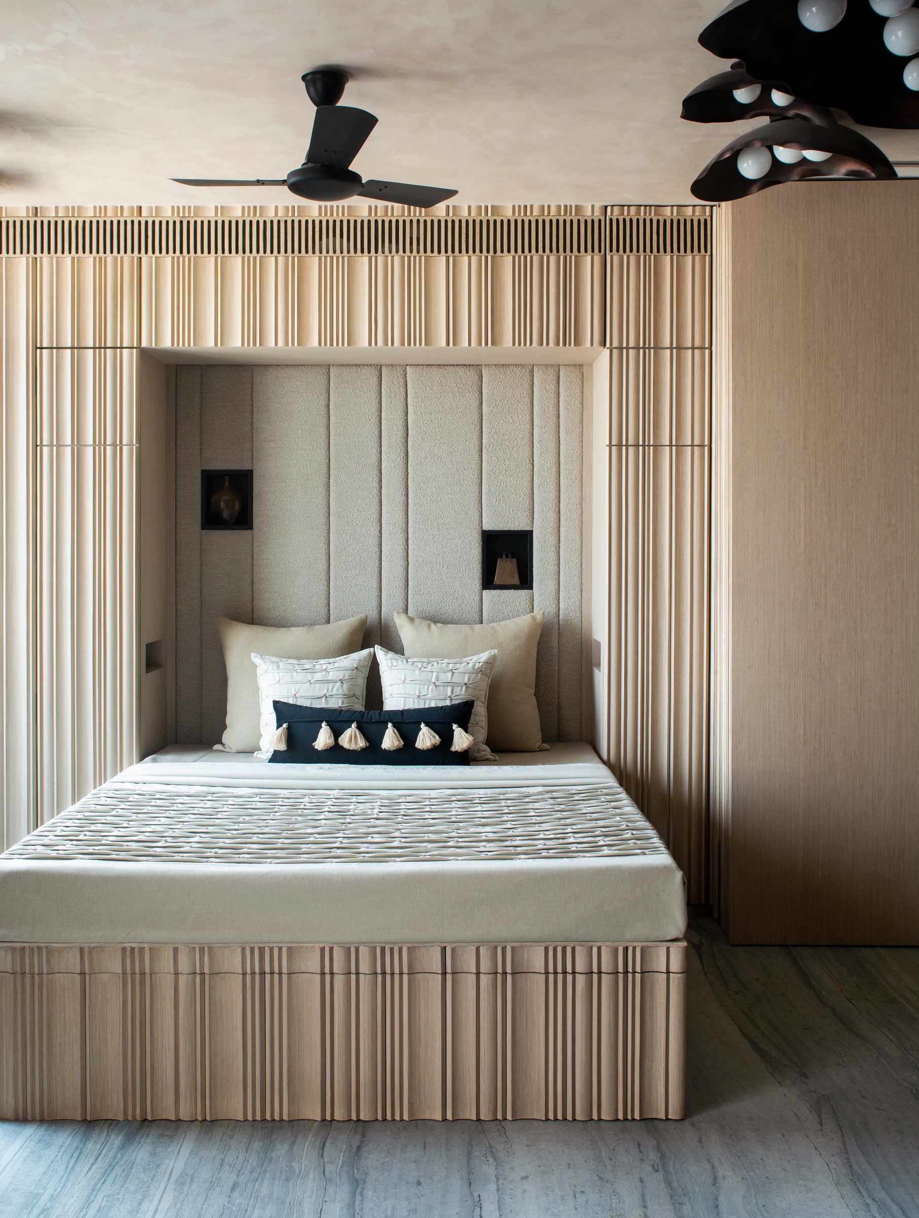 The first bedroom: a recessed alcove framed by fluted wood-grain millwork, with a sculptural dark pendant overhead