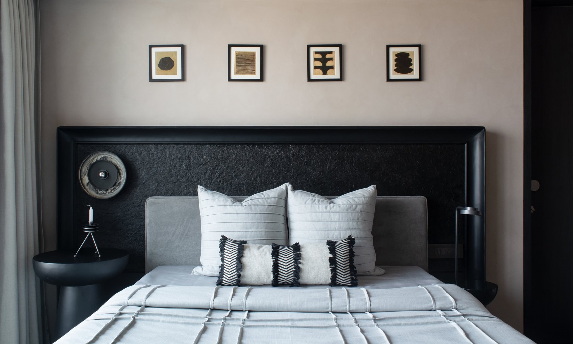 Another bedroom anchored by a dark framed headboard with a textured black inset, beneath four small framed works in a precise horizontal row