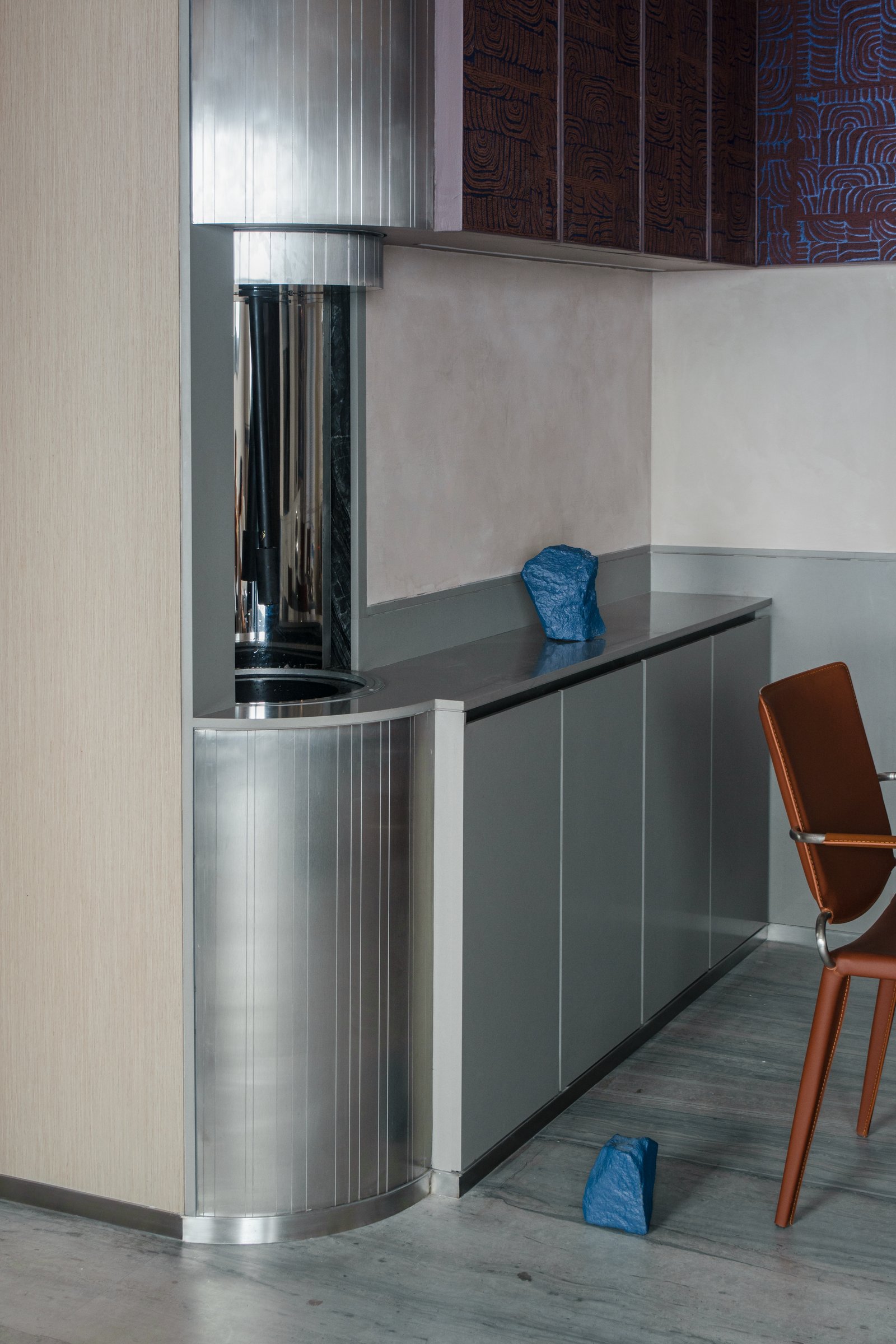 The service spine in grey lacquered cabinetry meets a fluted metallic column wrapping a structural element