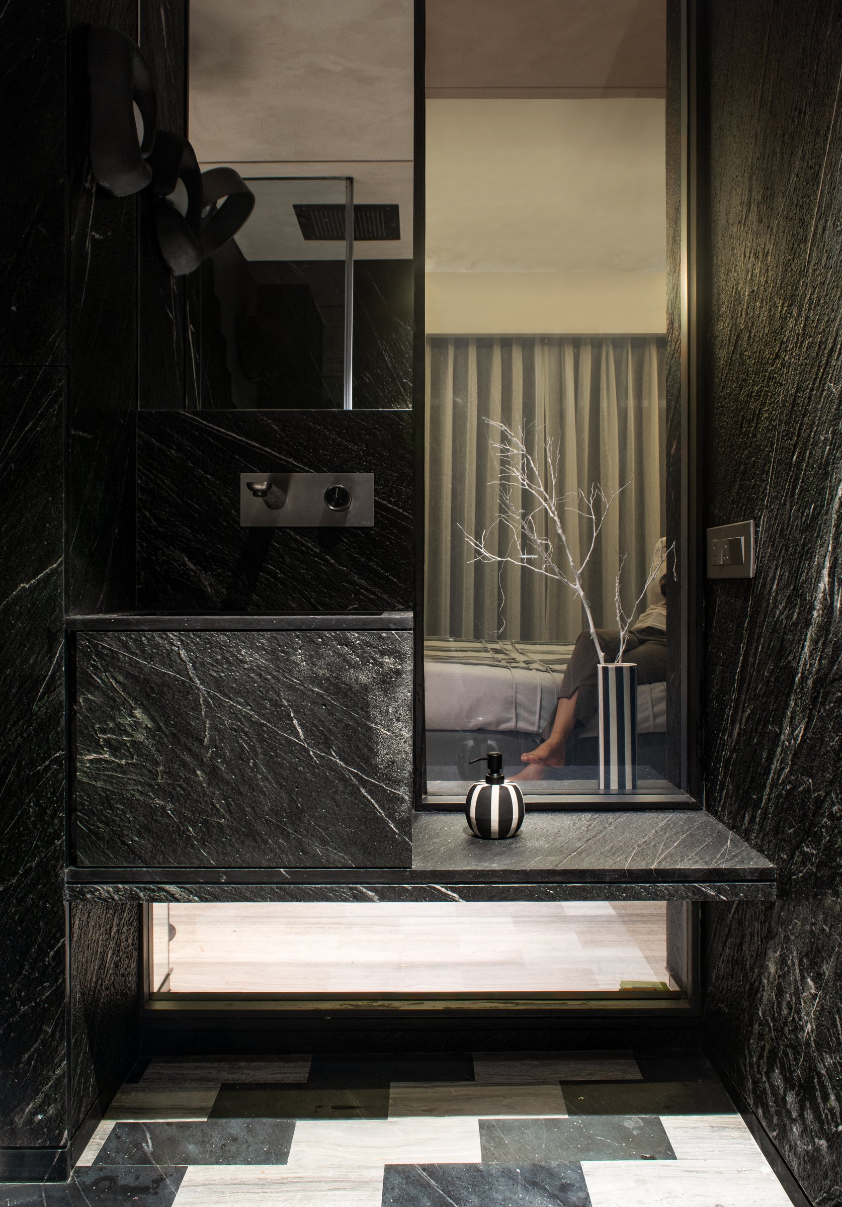 A second bathroom in veined black stone, where a vertical mirror frames a sightline back into the bedroom