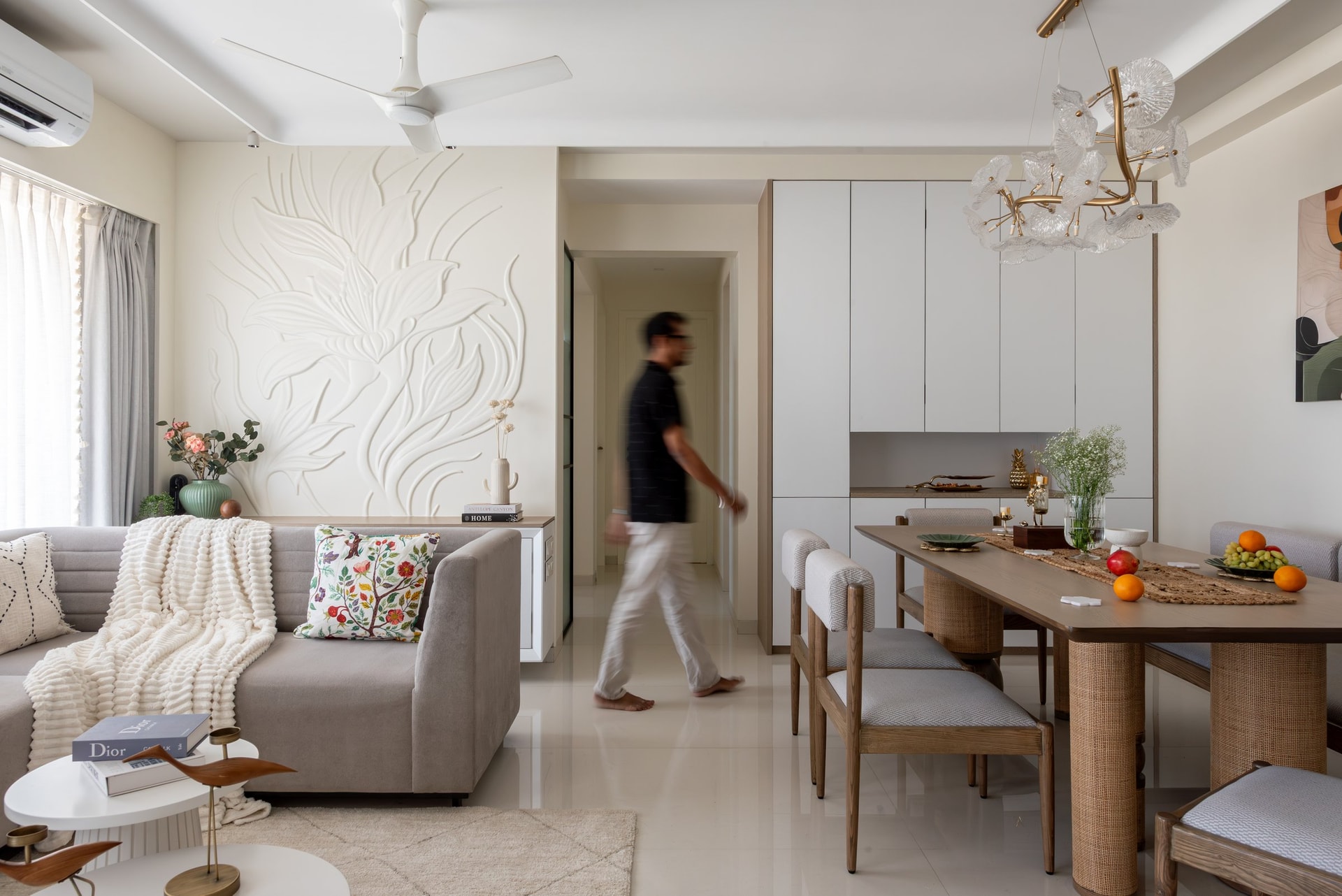 The living and dining zones read as one continuous interior, with a sculptural glass-and-brass chandelier as the single extravagant gesture