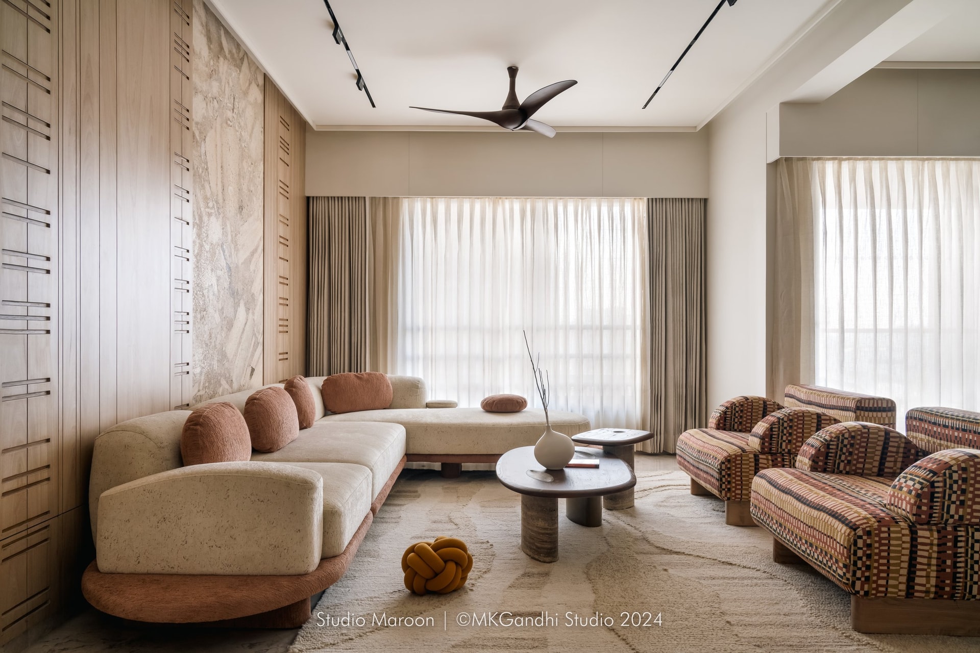 The living room anchored by a curved travertine-toned sofa, set against a slatted wood and natural stone feature wall