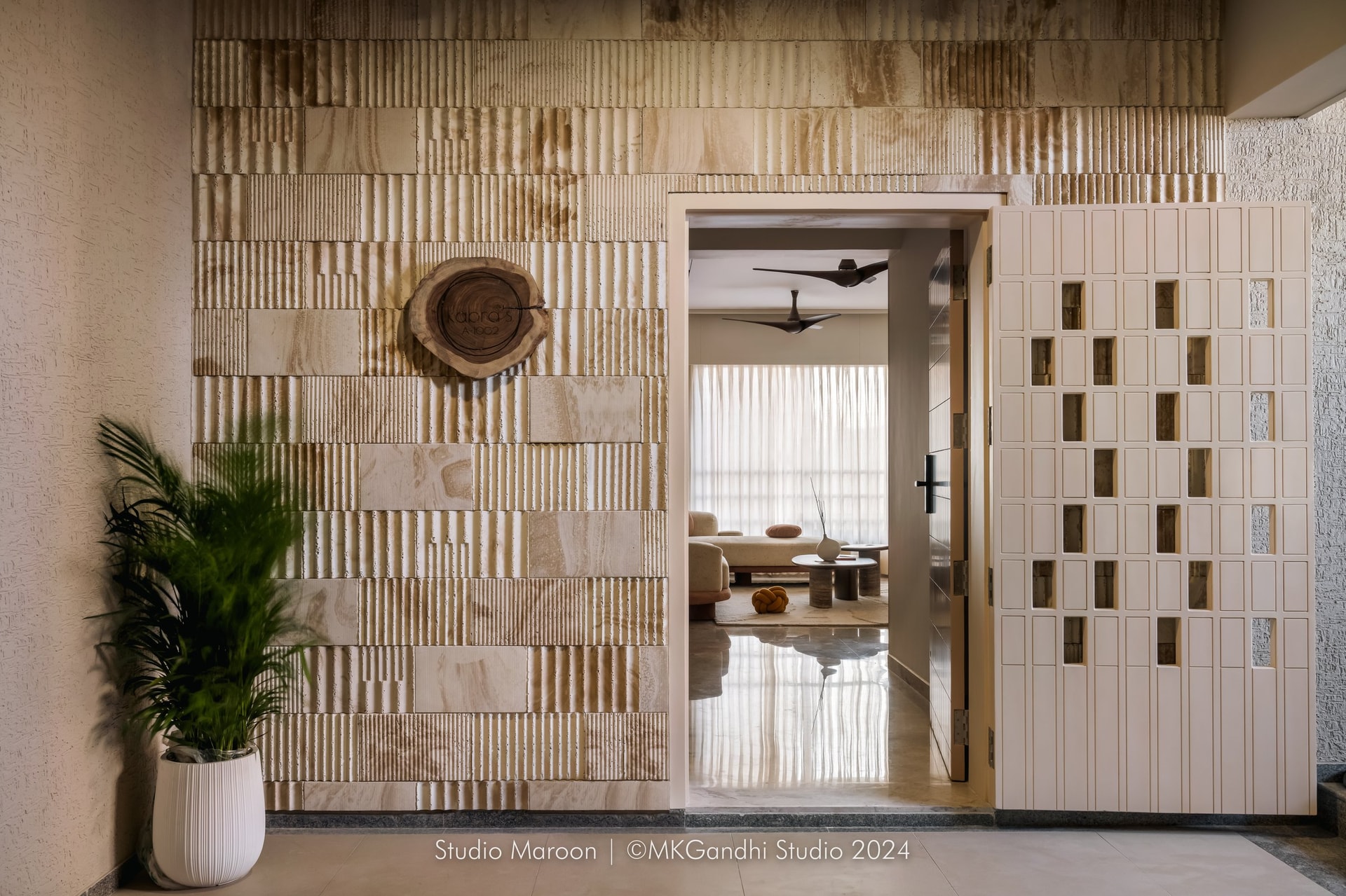 The entry: fluted stacked-stone cladding and a perforated screen door establish the home's material grammar before the rooms fully begin