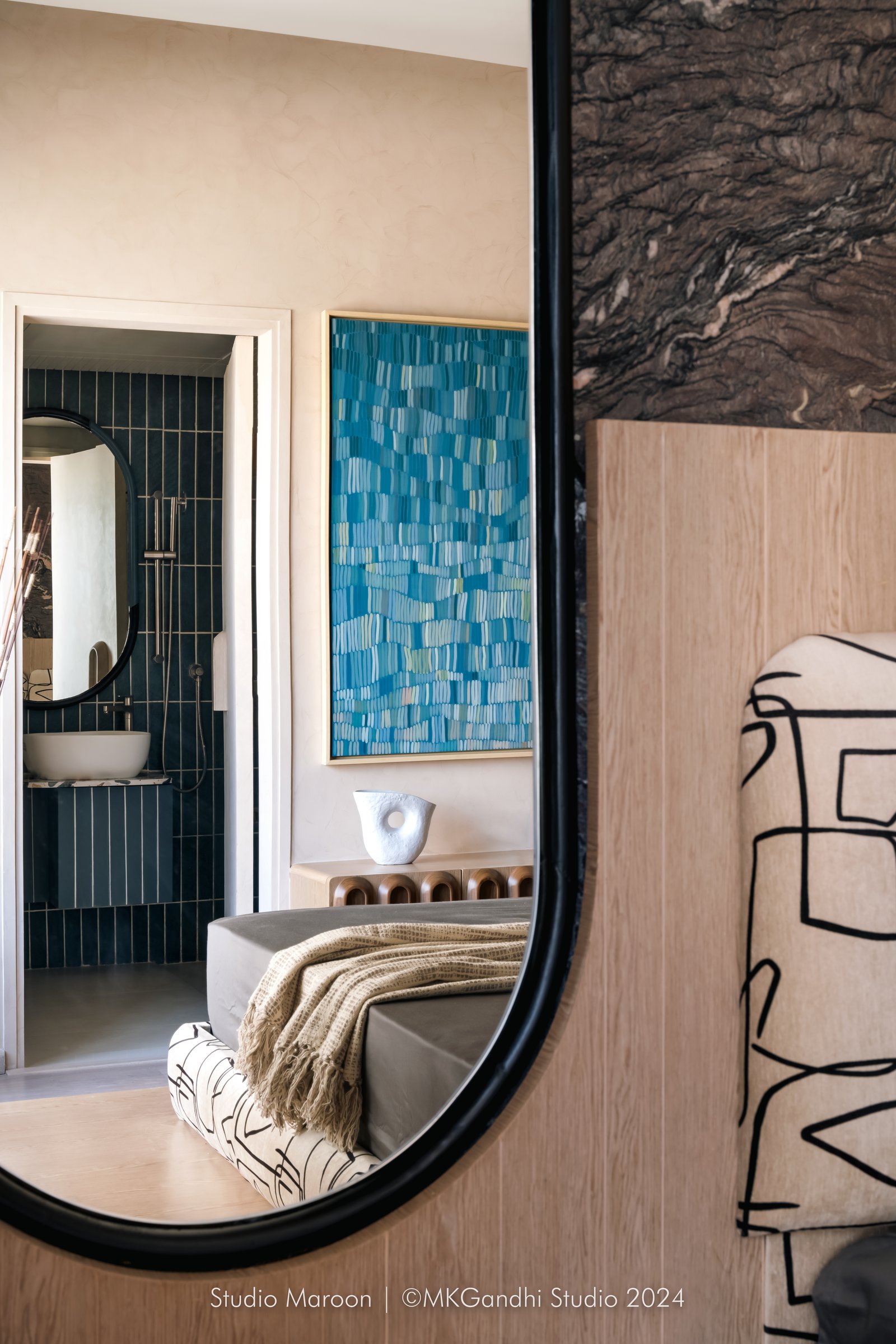 Through the oval mirror, a glimpse of the master bathroom in dark slim-tile cladding