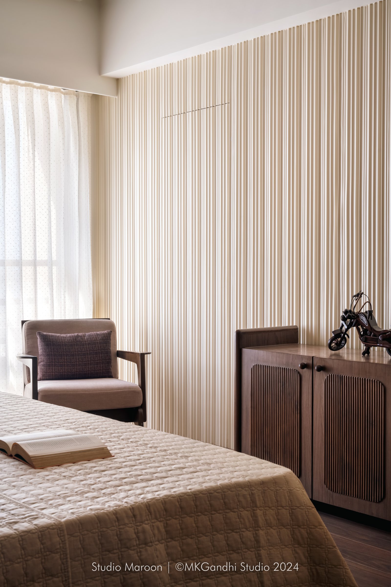 A third bedroom, where reeded walls meet warm flooring and a dusty pink linen armchair
