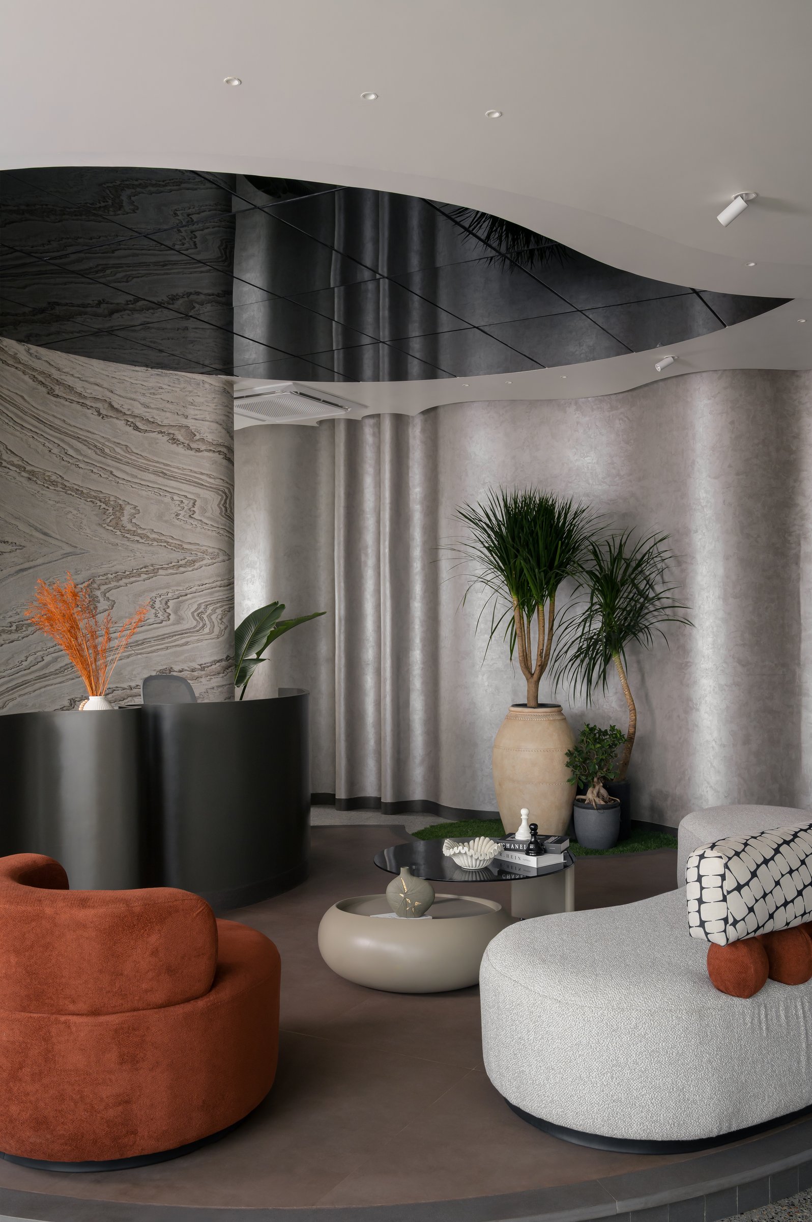 The reception lounge, where a terracotta swivel chair and patterned bench frame the curved platform against softly textured grey walls
