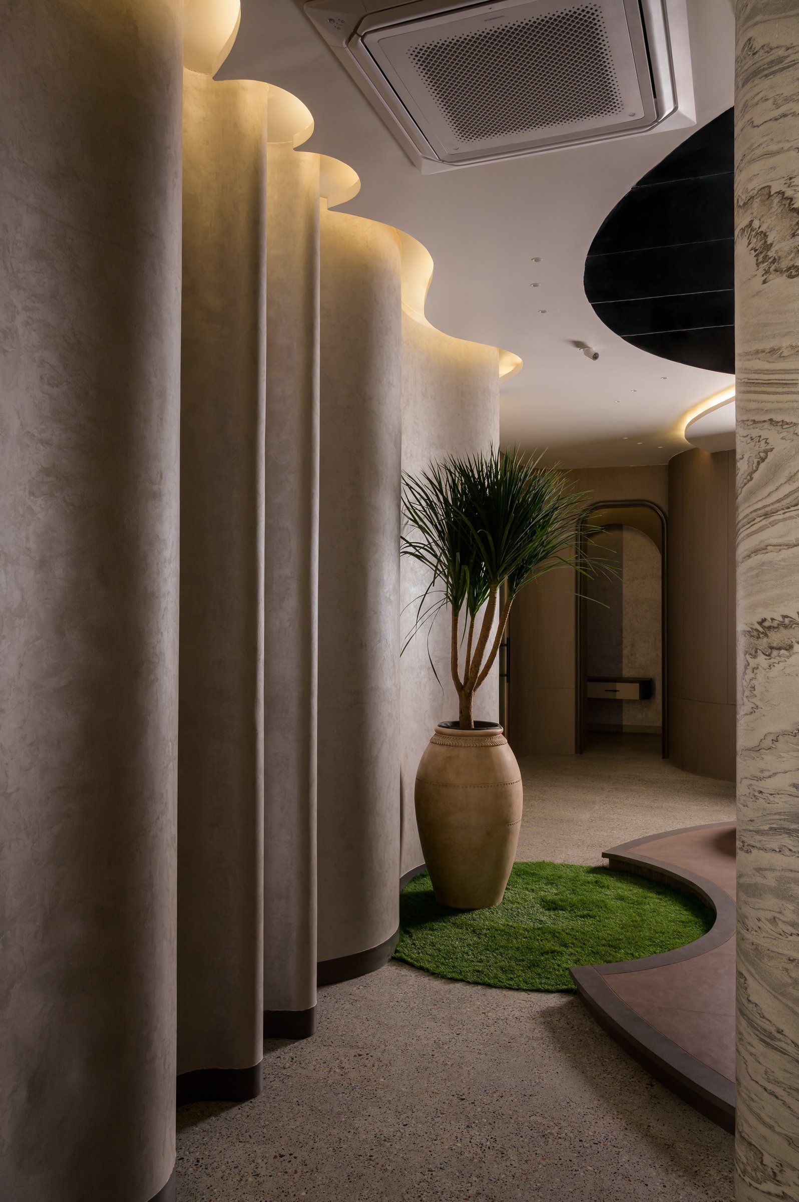 The circulation spine, where scalloped plaster volumes lit from above choreograph the passage between zones
