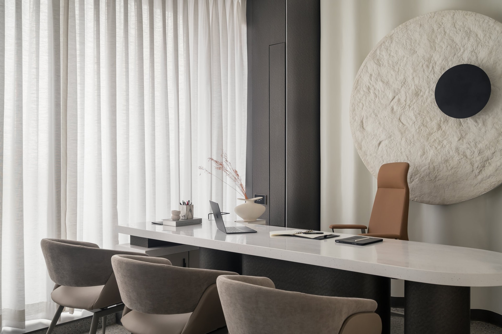 The director's office, where sheer ivory drapes and a textured circular relief frame a long composite-stone desk