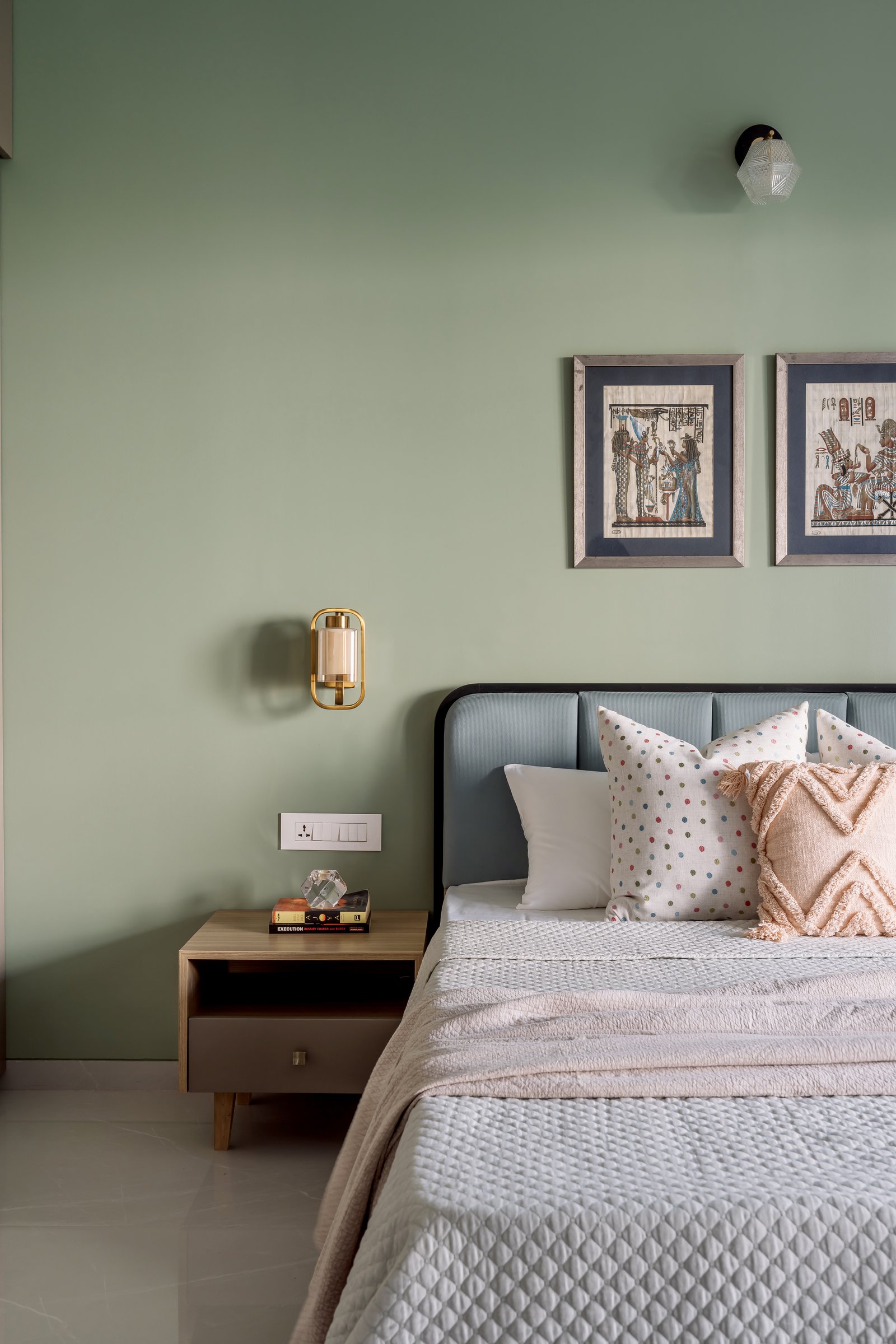 The second bedroom, where a sage wall and framed prints hold the room's quieter register