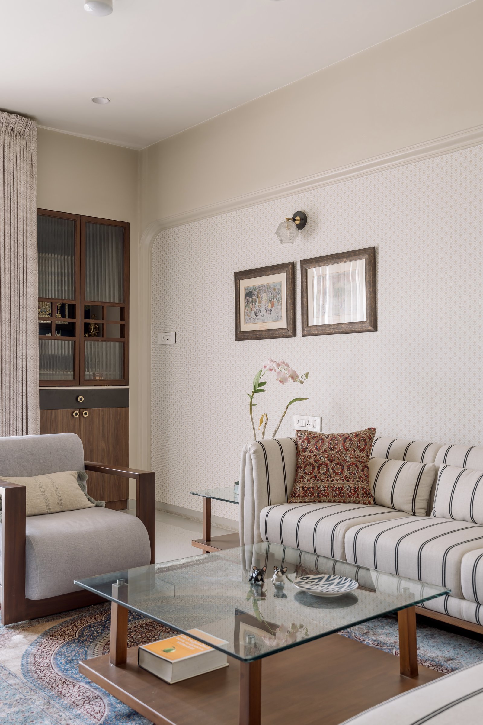 The TV and puja room, where a striped sofa and refurbished teak armchair share a quiet patterned wall