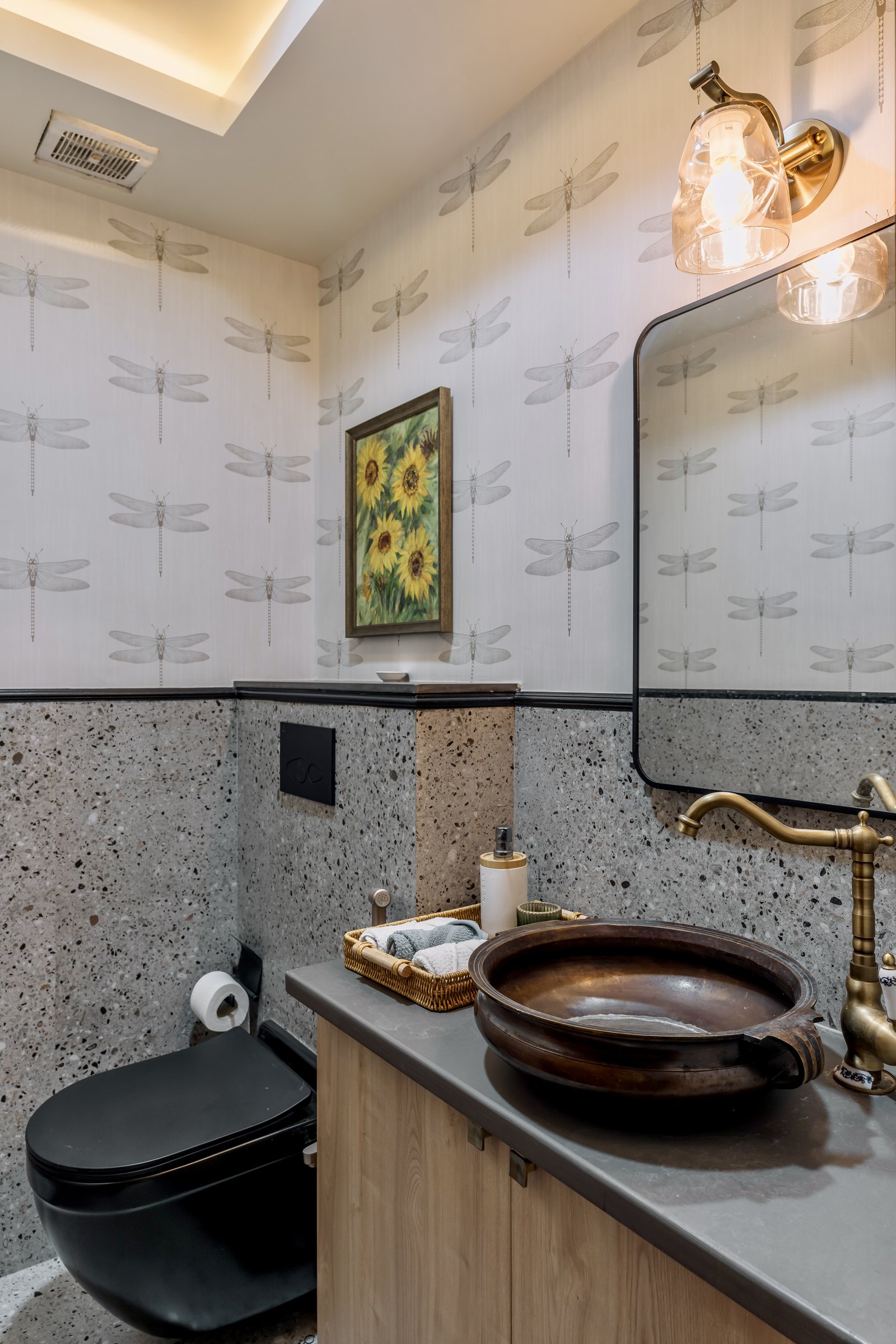 The powder room, where a bronze uruli basin sits on a contemporary stone counter beneath patterned wallpaper