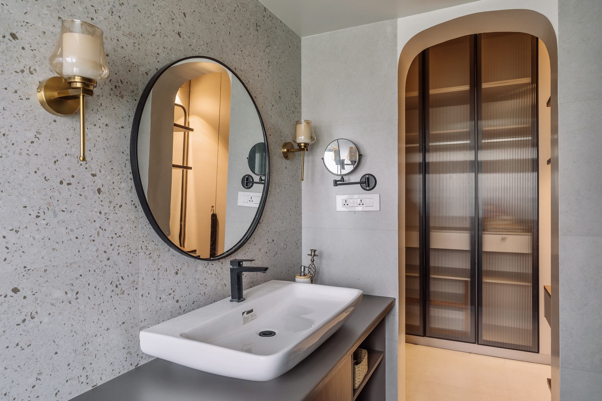 An adjoining bathroom, where a terrazzo wall and an arched fluted-glass partition continue the home's recurring motifs