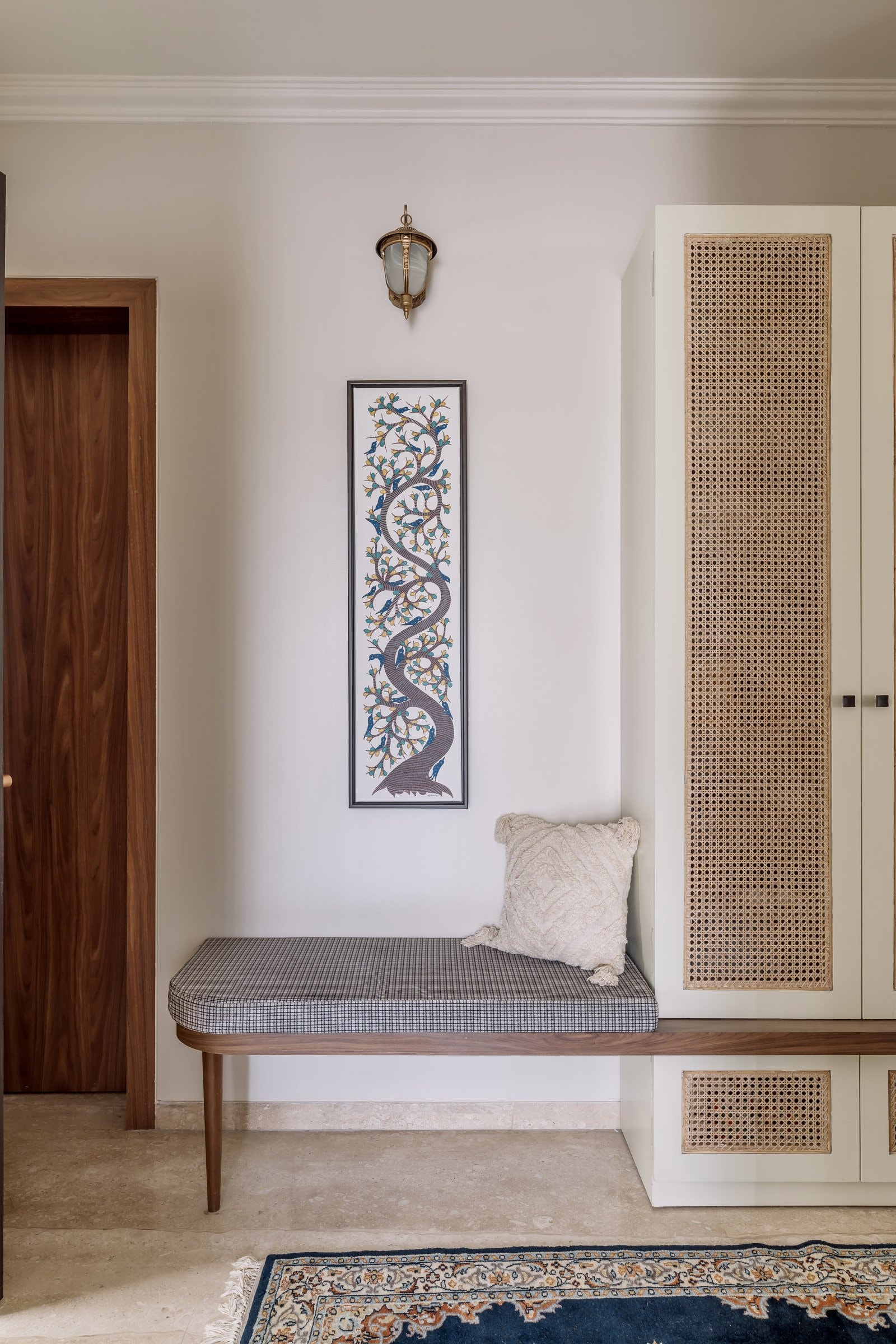 The entry, where a Gond-style painting and a cane-fronted wardrobe set the home's material grammar