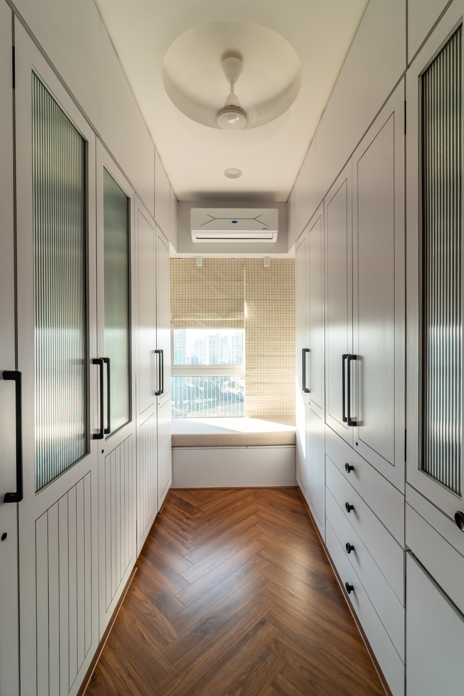 The dressing corridor: floor-to-ceiling wardrobes line both walls, terminating in a window seat at the far end