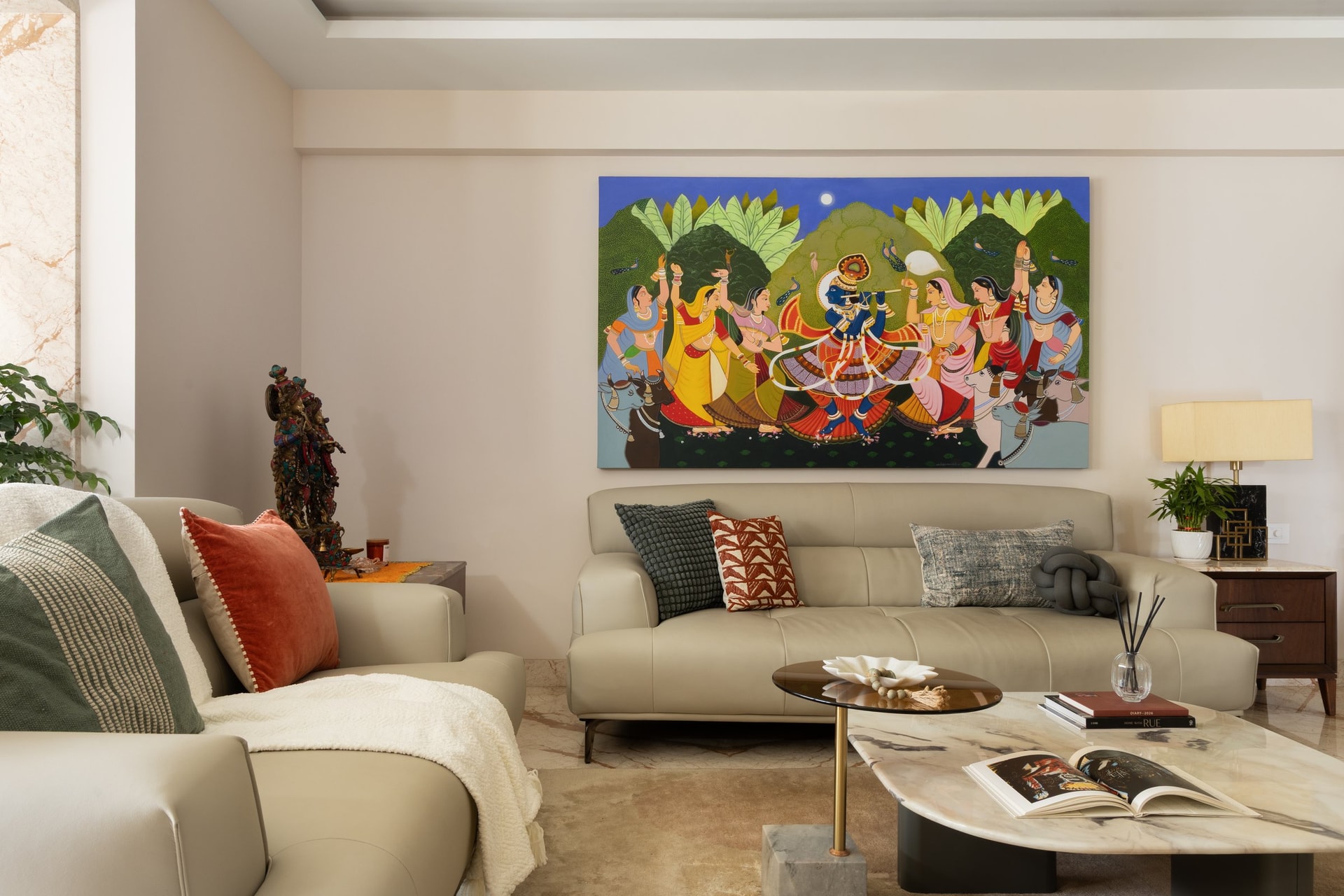 The living room square-on: a low sectional, a small bronze deity at the sofa's edge, and a cushion palette that quietly echoes the painting above